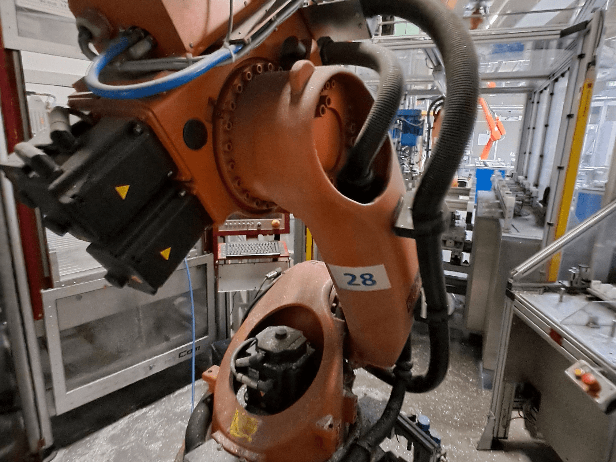 Nahaufnahme des KUKA KR30-3-Roboterarms mit orangefarbenem Gehäuse, gekennzeichnet mit der Nummer 28; aus der Seitenansicht sind die Motoren und die Verkabelung zu sehen.