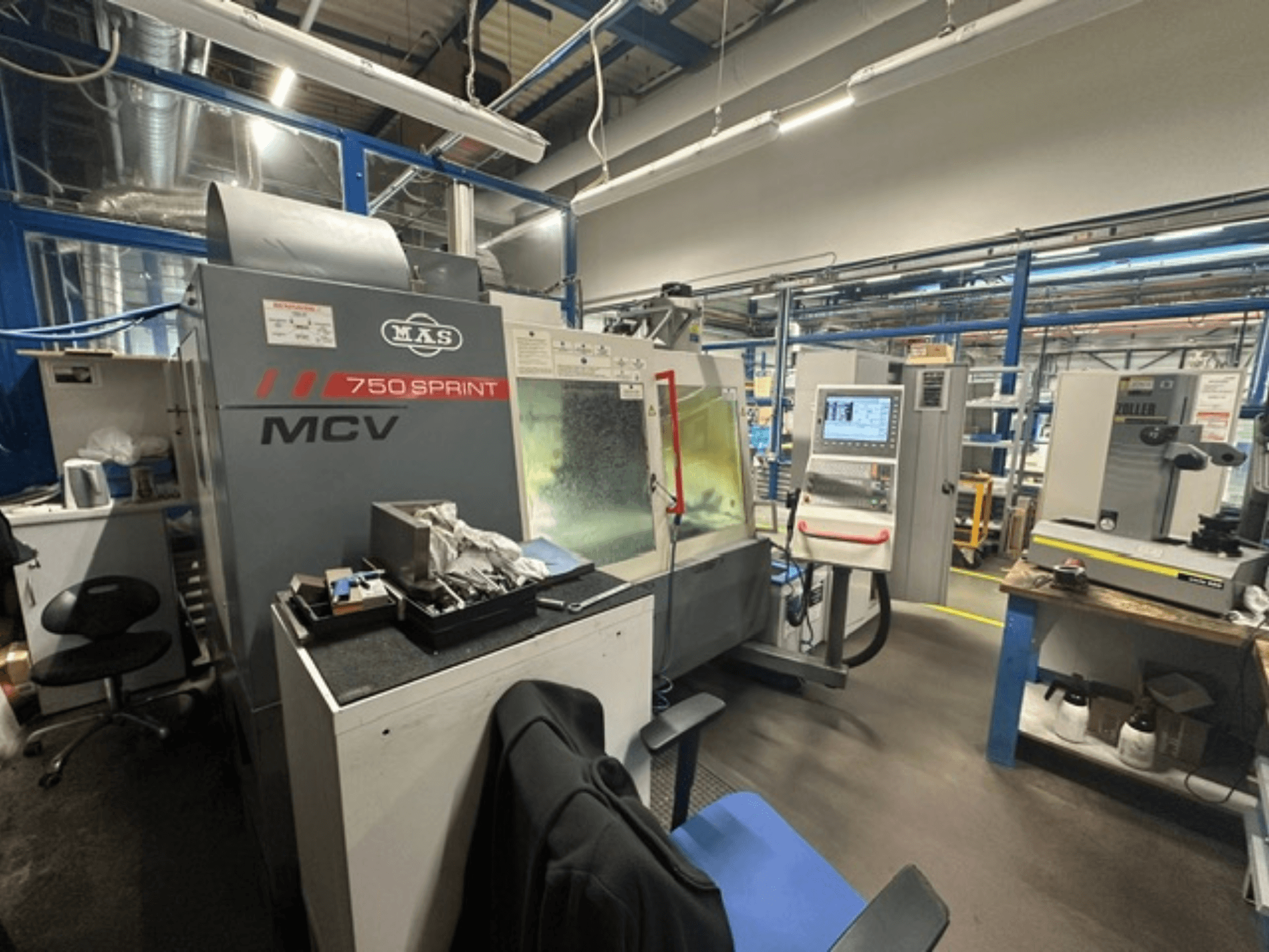 Vertikales Bearbeitungszentrum KOVOSVIT MAS MCV 750 Sprint in einer Werkstatt, mit seitlicher Ansicht auf das Bedienfeld und den Arbeitsbereich.