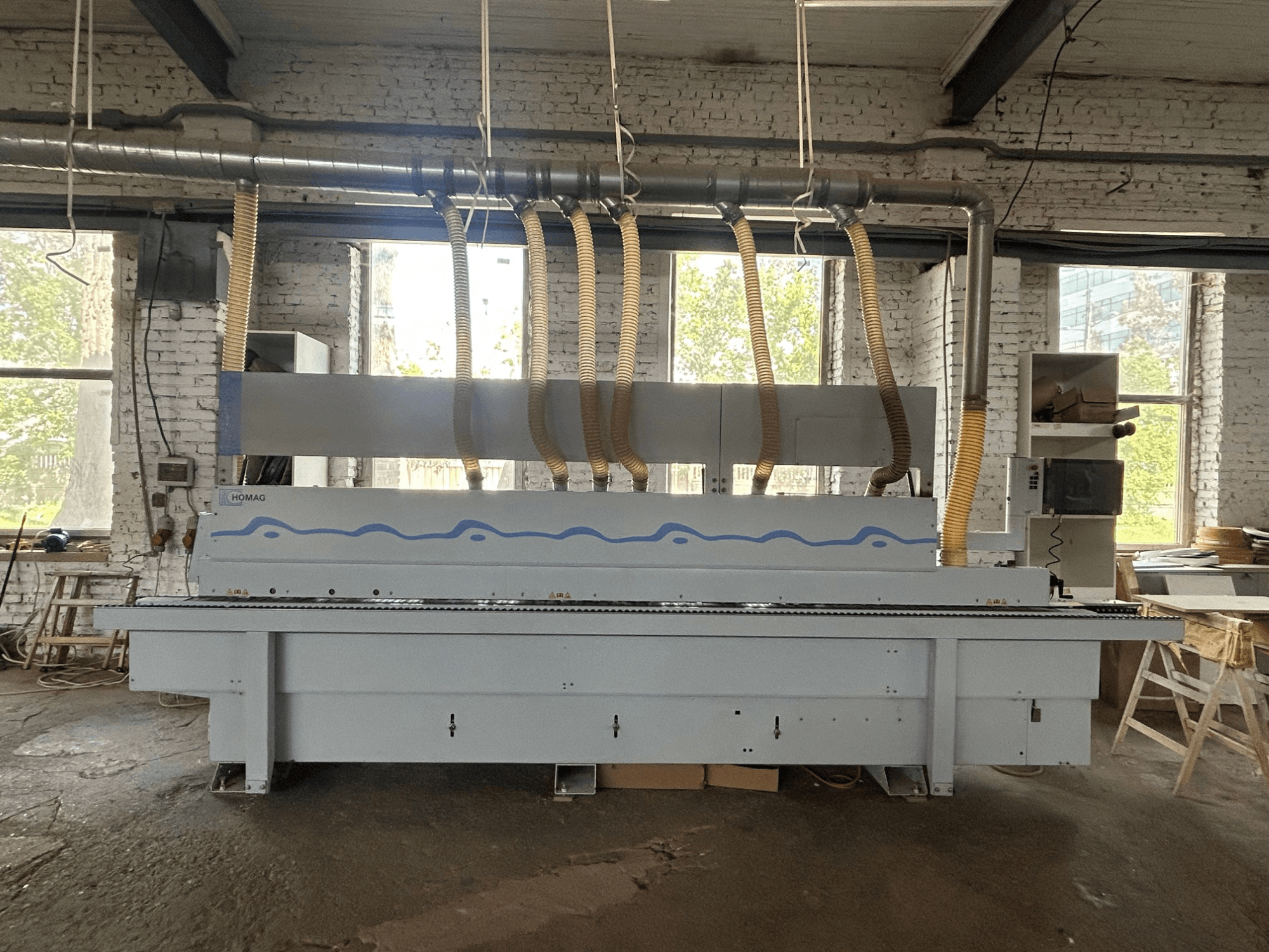 Vorderansicht der Kantenanleimmaschine HOMAG Optimat KDF 440 C, die eine große Maschine mit Absaugschläuchen und einem Bedienfeld zeigt.
