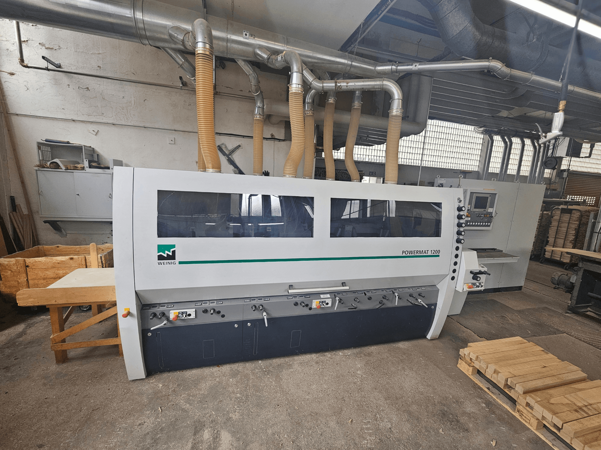 Weinig Powermat 1200 Holzbearbeitungsmaschine, Vorderansicht, mit Bedienfeld und Holzstapeln in einer Werkstattumgebung.