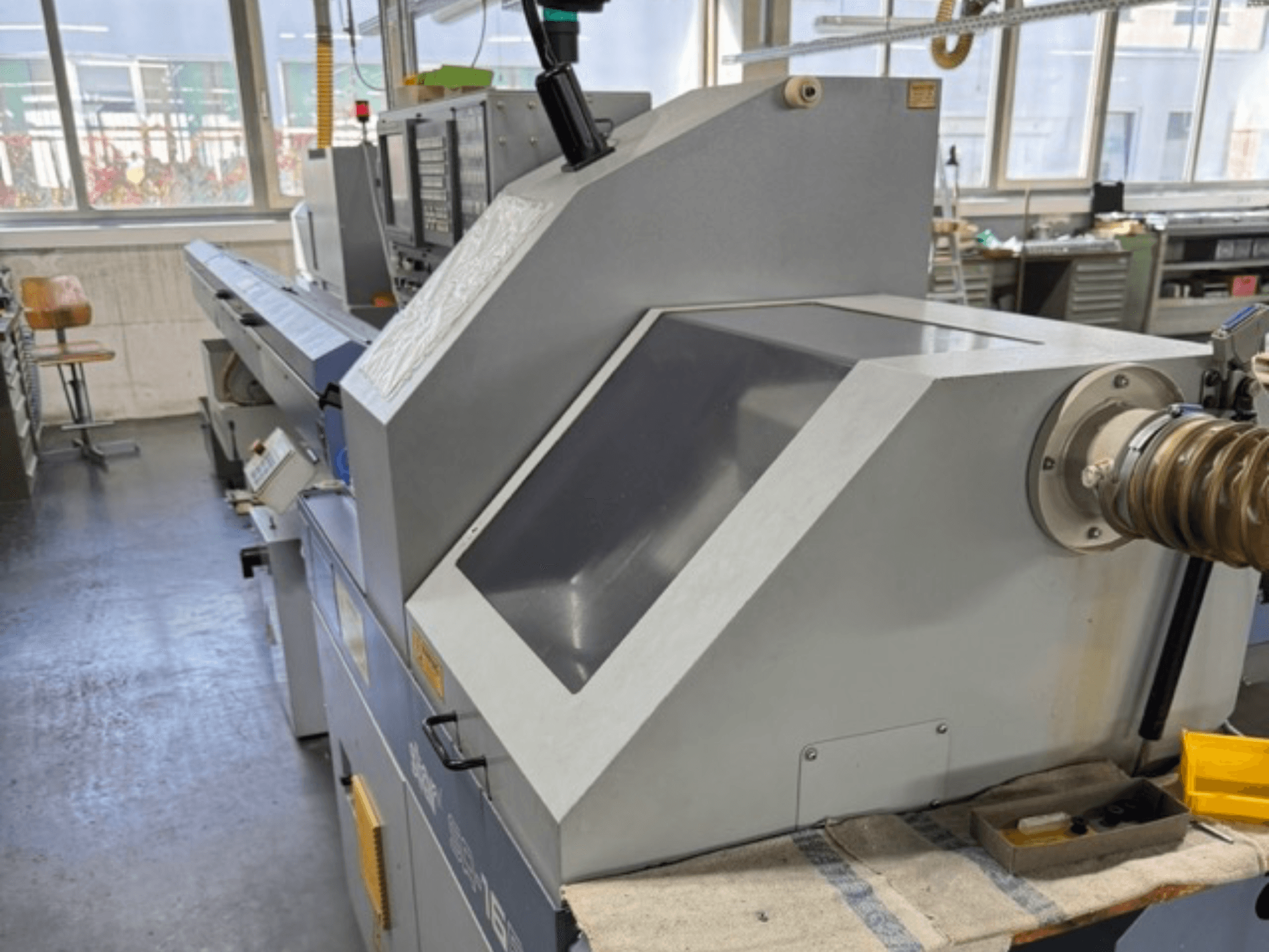 Graue Industriemaschine, von der Seite betrachtet, mit großem, abgewinkeltem Bedienfeld, Steuertasten und Schlauchaufsatz.