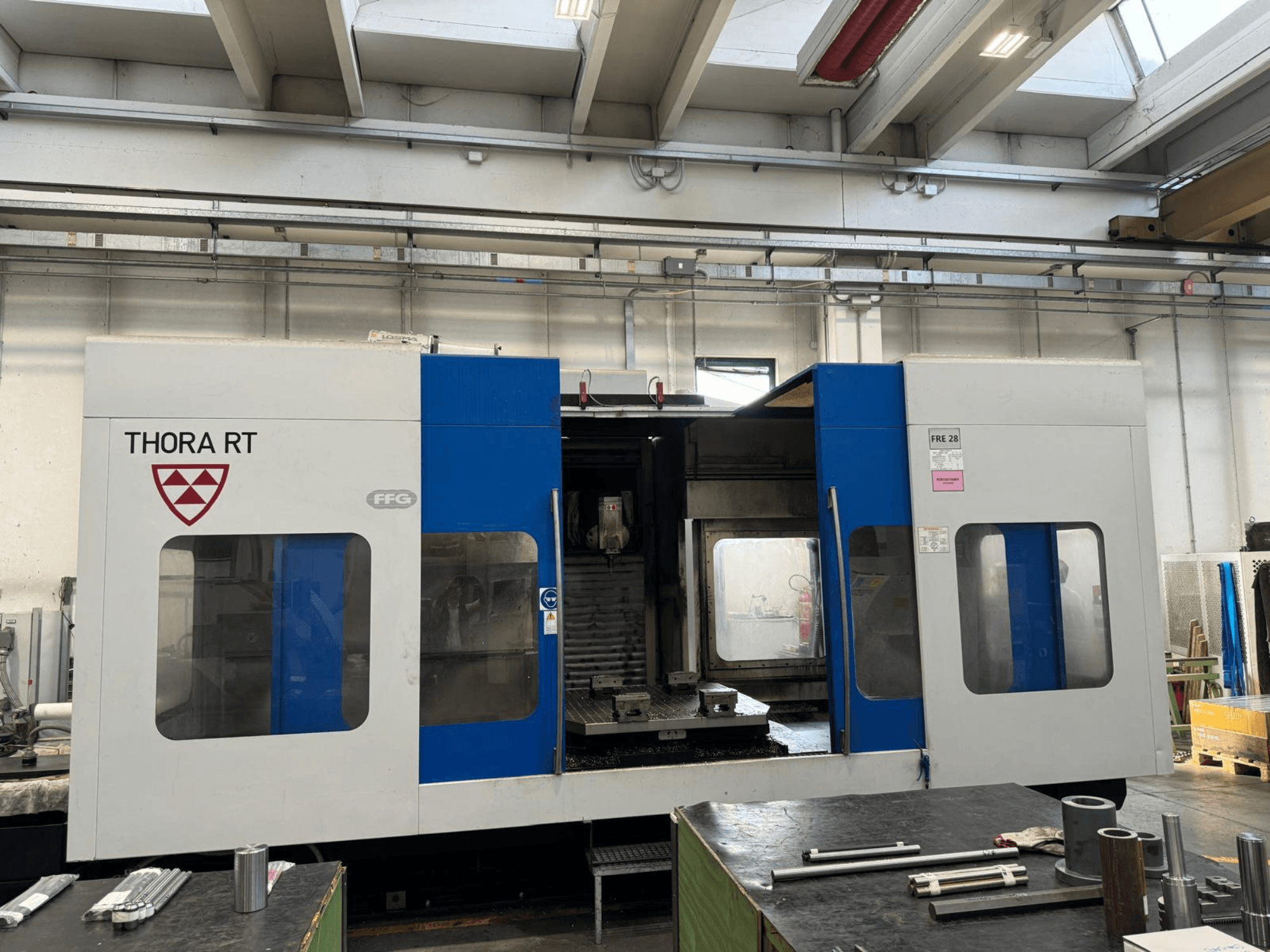 CNC-Maschine THORA RT von vorne gesehen, mit blau-weißem Äußeren, transparenten Fenstern und montierten Werkzeugen.
