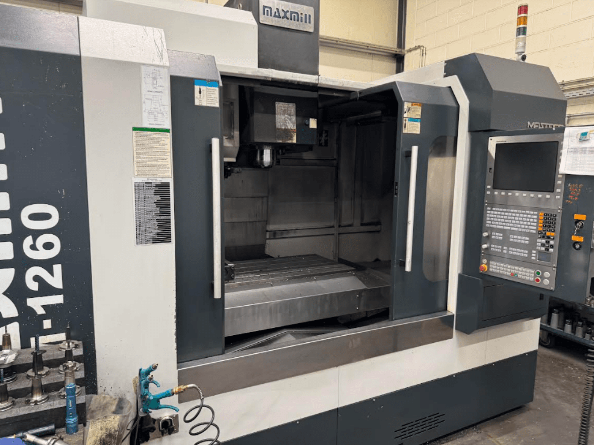 Maxmill CNC-Fräsmaschine, Modell M-1260, Vorderansicht mit leerem Arbeitsbereich, Bedienfeld und Betriebsanleitung.