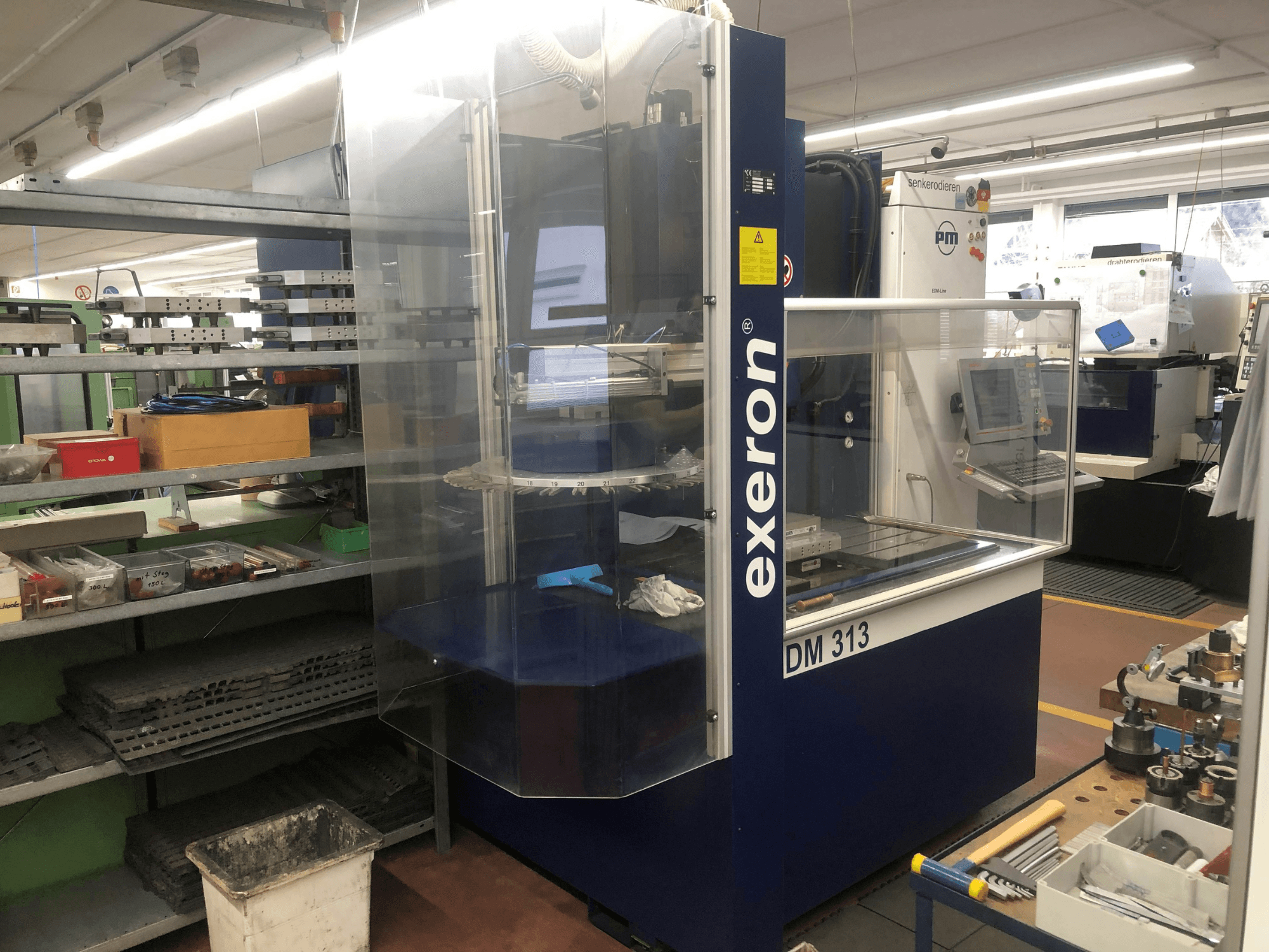 Exeron EDM 313 Senkerodiermaschine in einer Werkstatt, Vorderansicht mit durchsichtigem Gehäuse und Bedienfeld.
