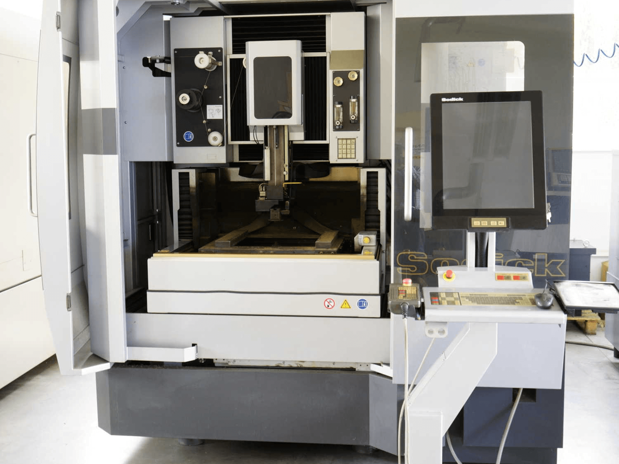 Vorderansicht der Sodick SLC400G-Drahterodiermaschine, auf der das Bedienfeld, der Arbeitsbereich und die inneren Mechanismen deutlich zu erkennen sind.