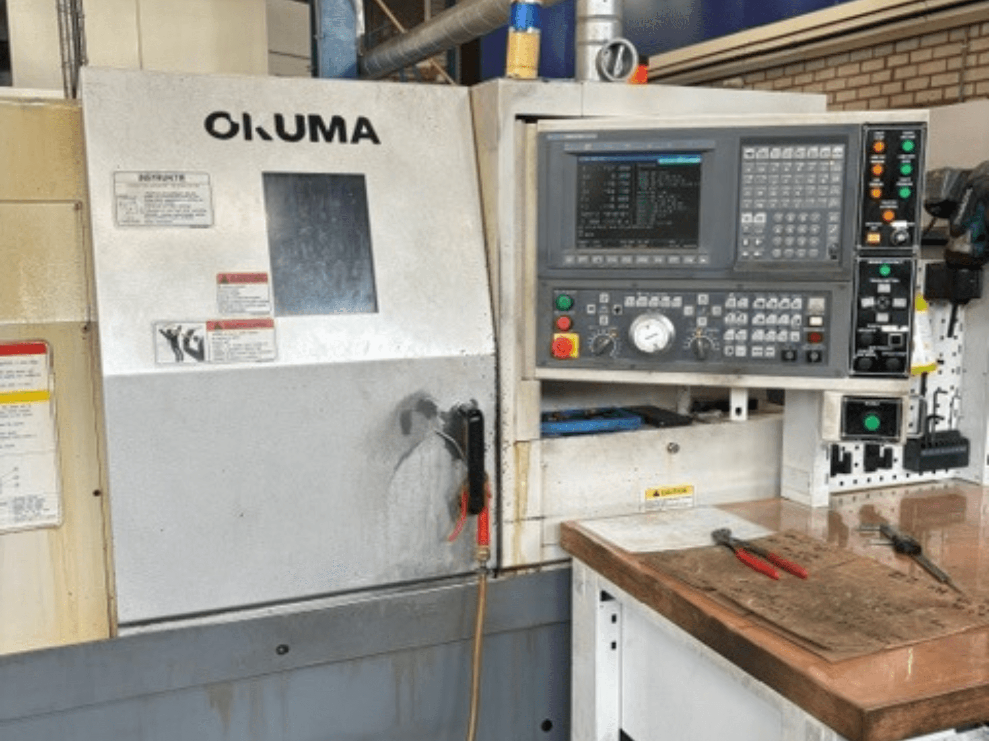 Frontansicht der Horizontal-Drehmaschine Okuma ES-L10II mit Bedienfeld, Display und Arbeitsbereich mit Werkzeugen.