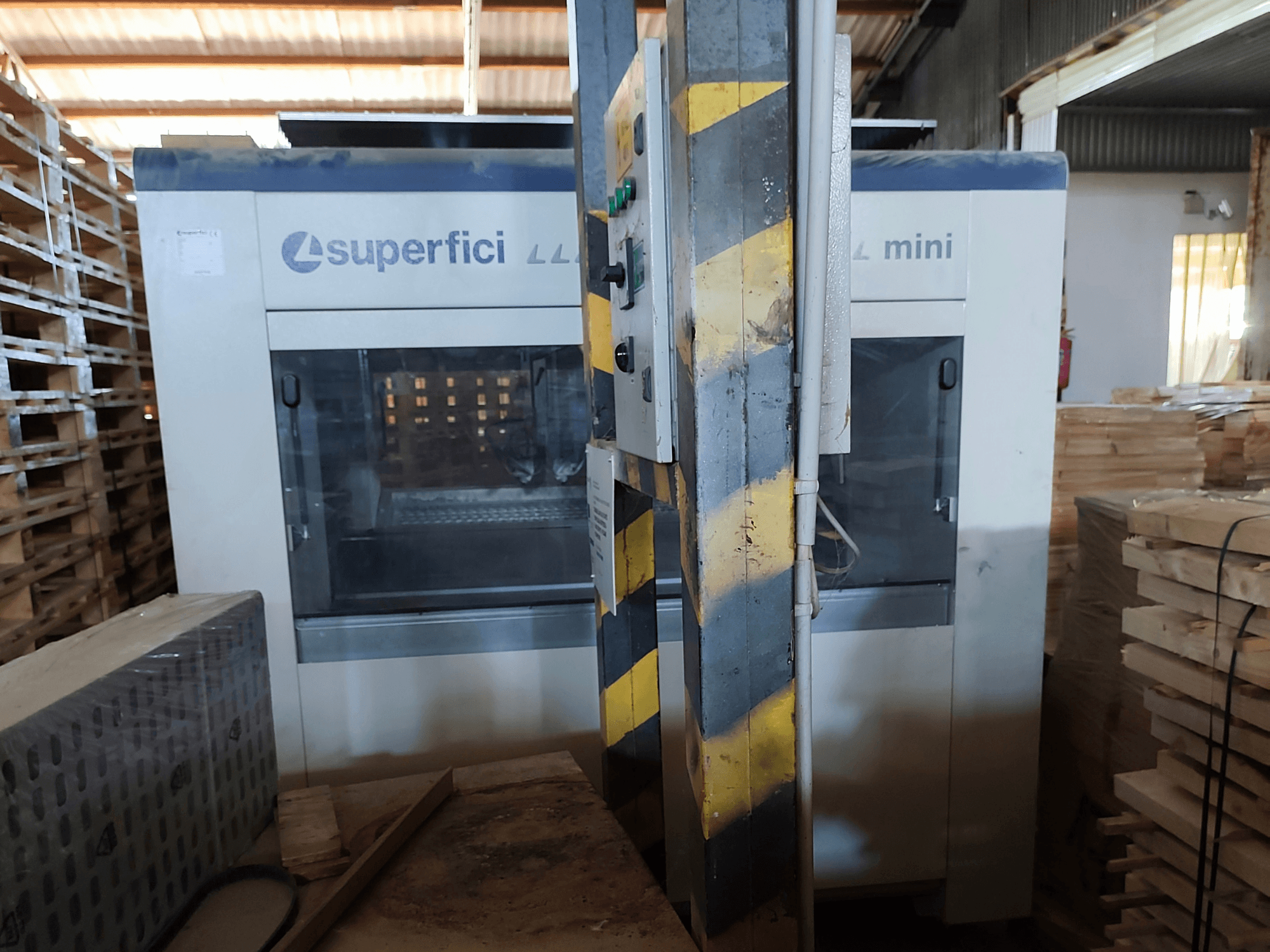 Die Holzveredelungsmaschine „SCM Superfici Mini“ in der Vorderansicht, mit Blick auf das Bedienfeld und die umliegenden Holzpaletten.