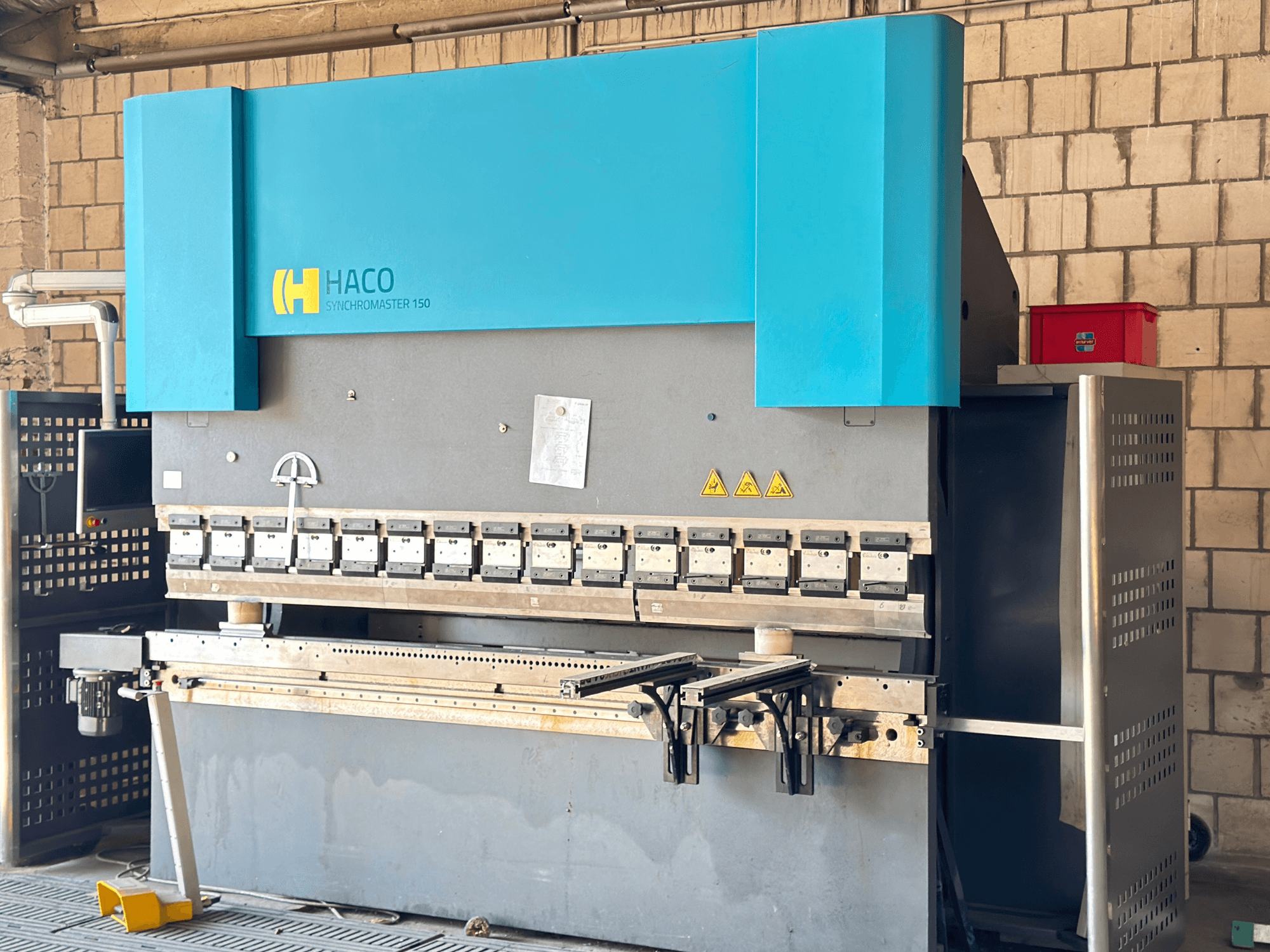 Abkantpresse HACO SRM30150, Vorderansicht; mit Bedienfeld und Spannwerkzeugen, mit sichtbaren Sicherheitswarnschildern.