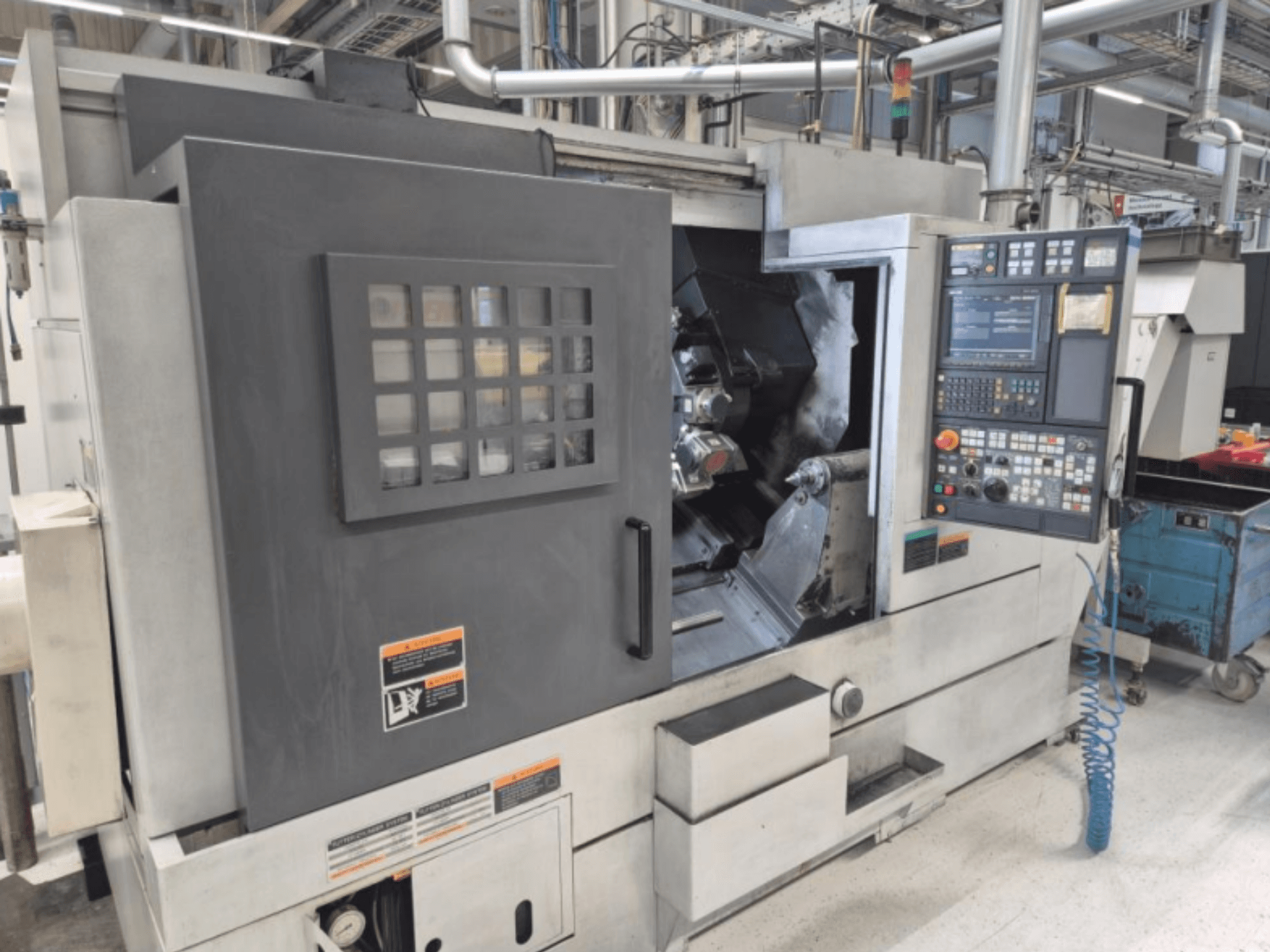 CNC-Drehmaschine mit Bedienfeld, Vorderansicht. Mit sichtbarem Arbeitsbereich und Sicherheitsfenster, Marke unbekannt.