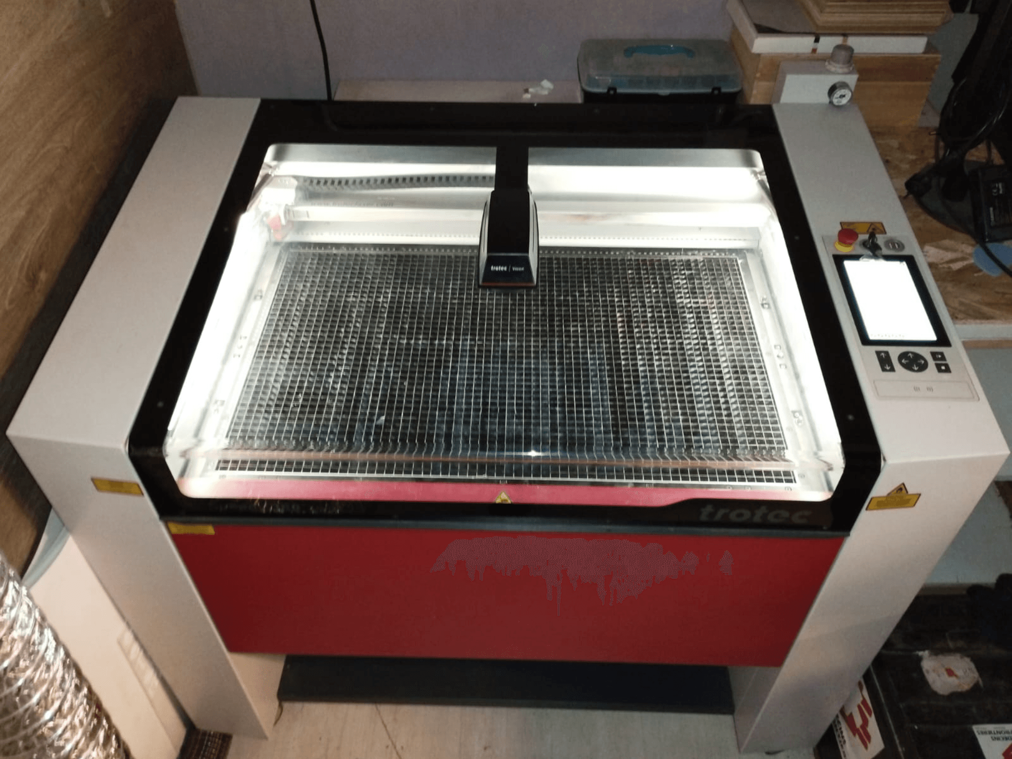 Trotec-Laserschneider mit transparentem Deckel, Gitterbett und Bedienfeld auf der rechten Seite; Frontansicht mit Darstellung von Design und Funktionen.