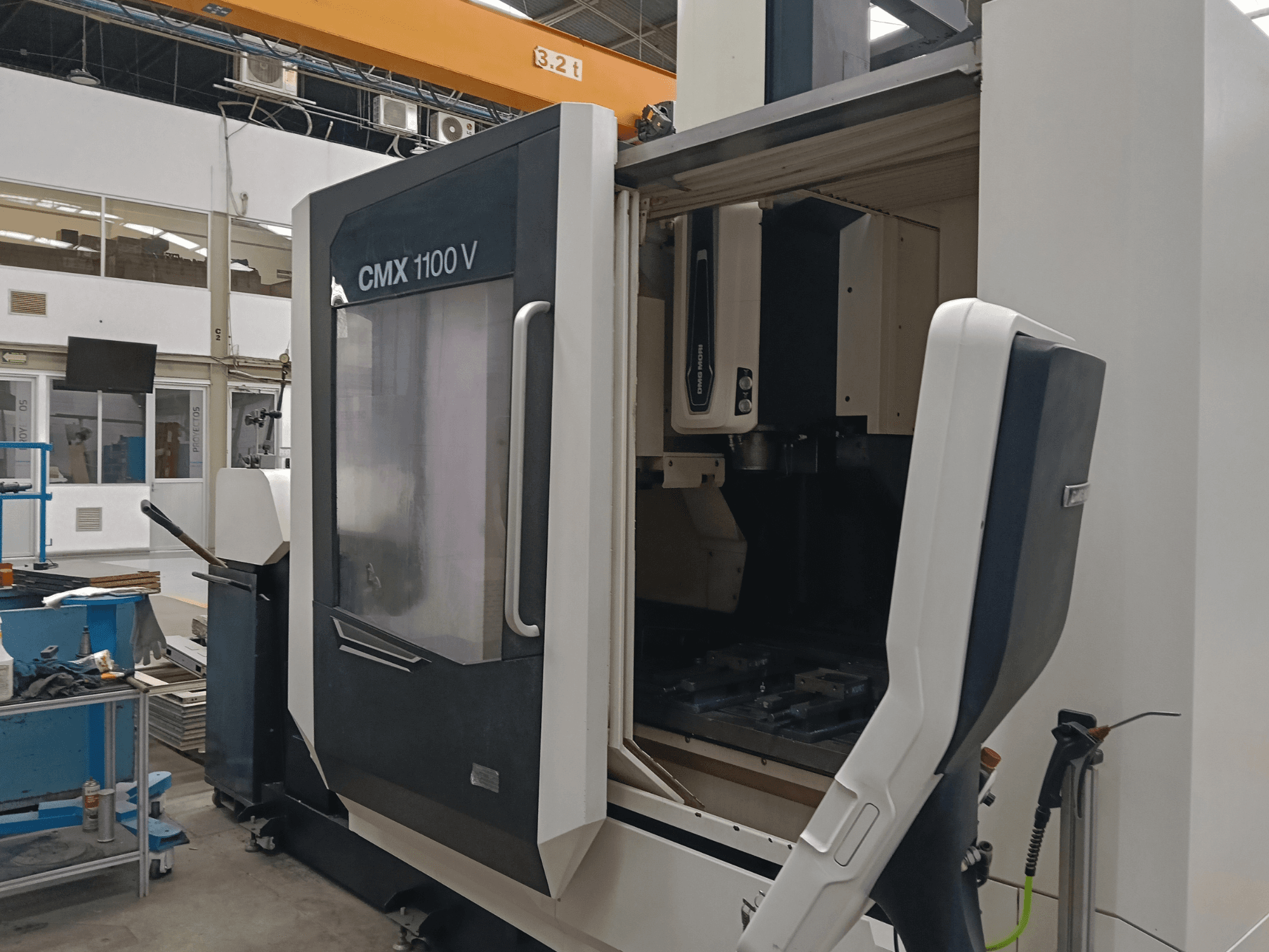 Vertikales Bearbeitungszentrum DMG MORI CMX 1100 V, Vorderansicht mit geöffneter Tür und Einrichtungsansicht des Werkzeugaufbaus in einer Industriehalle.