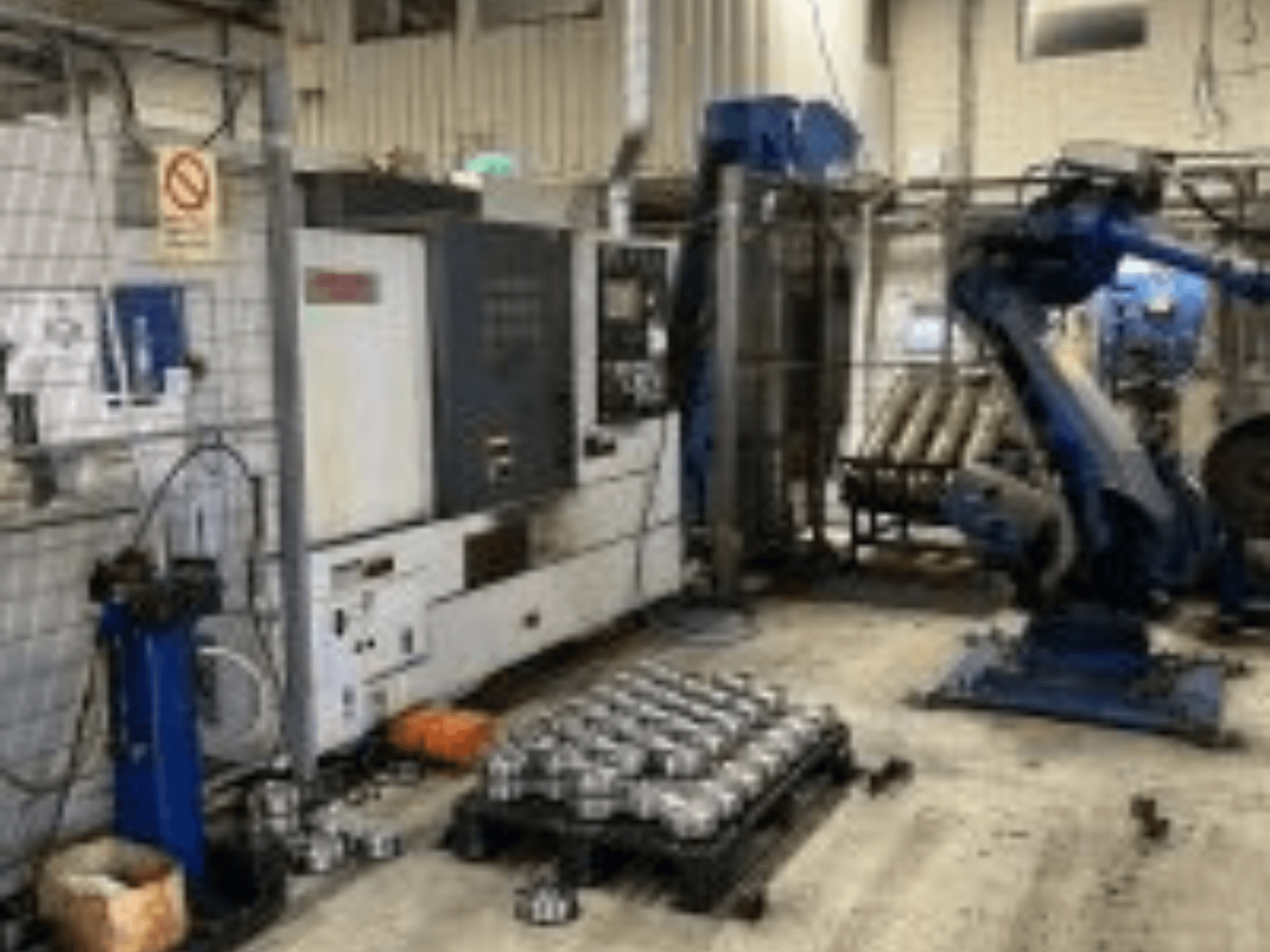 Horizontalansicht der MORI SEIKI NL 2500 MC/700 Drehmaschine mit Roboterarm und Metallteilen auf dem Boden.