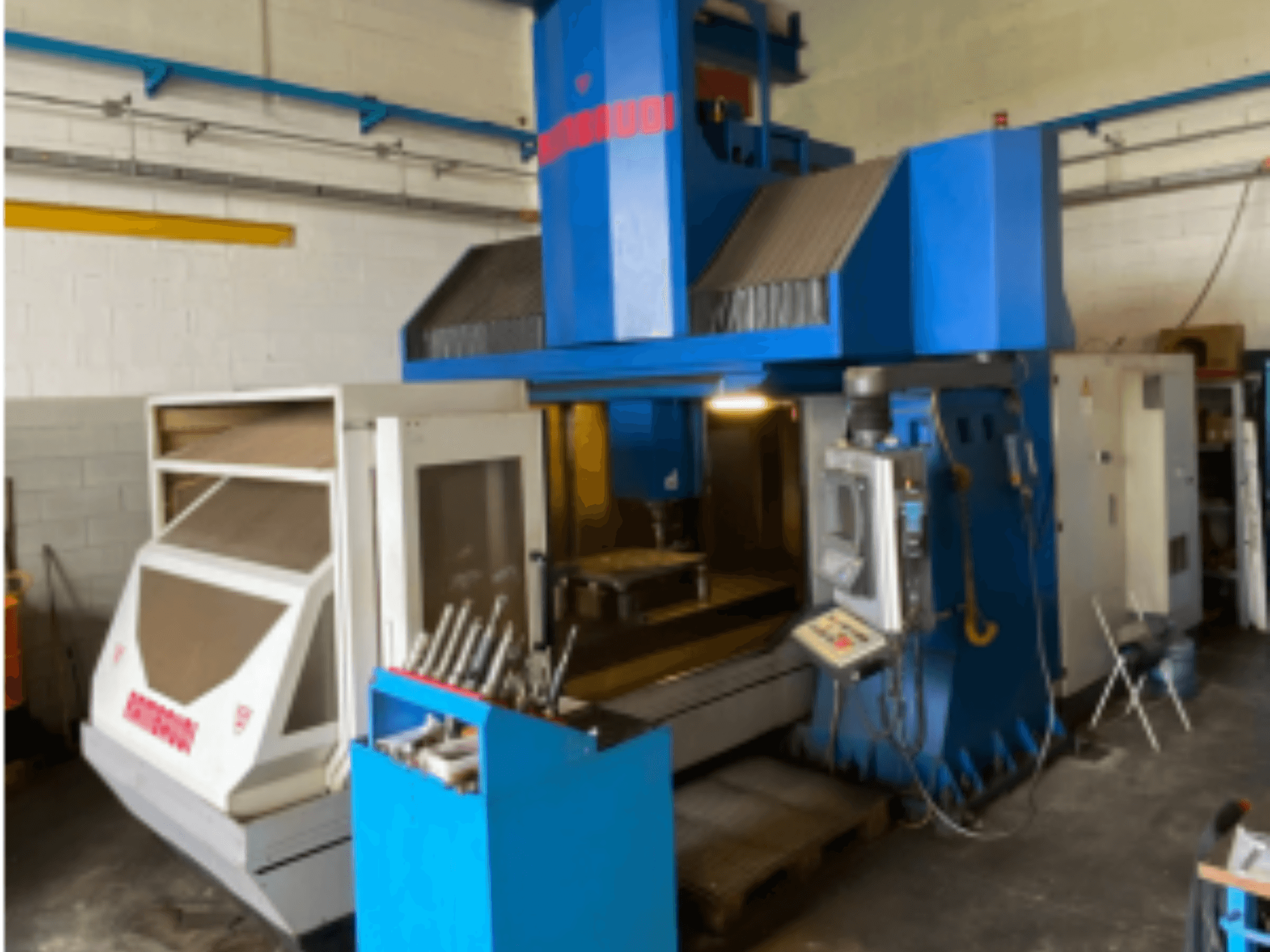 Vertikales Bearbeitungszentrum Rambaudi RF103, Vorderansicht mit Bedienelementen, Werkzeugablage und Bearbeitungsbereich. Außen blau und weiß.