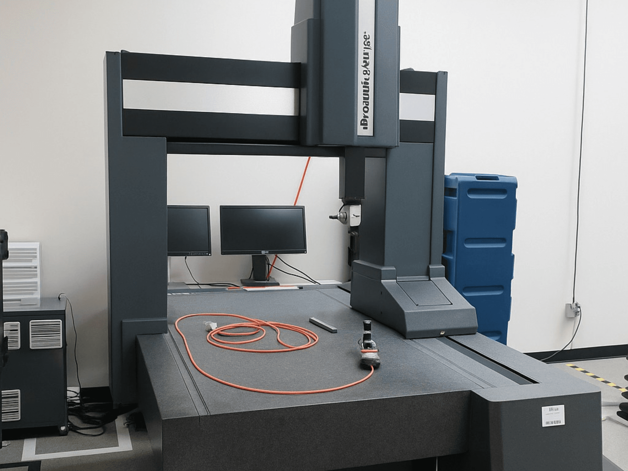 Brooks Automation Koordinatenmessgerät mit zwei Monitoren, Vorderansicht, mit grauer Tischplatte und Messwerkzeugen.