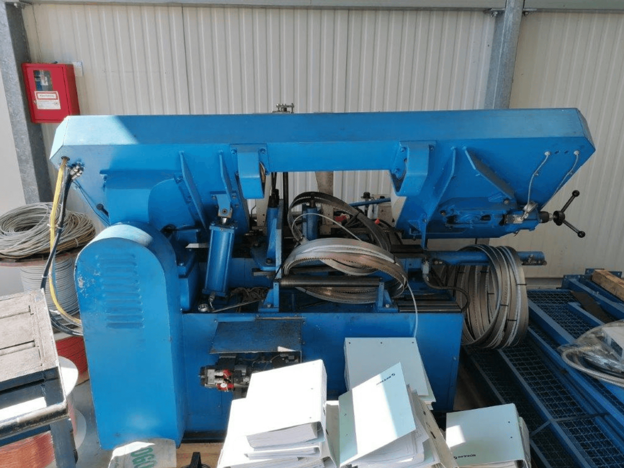 Blaue Industriemaschine mit hydraulischen Komponenten, Seitenansicht, umfasst Schläuche und Bleche auf einer Fläche.