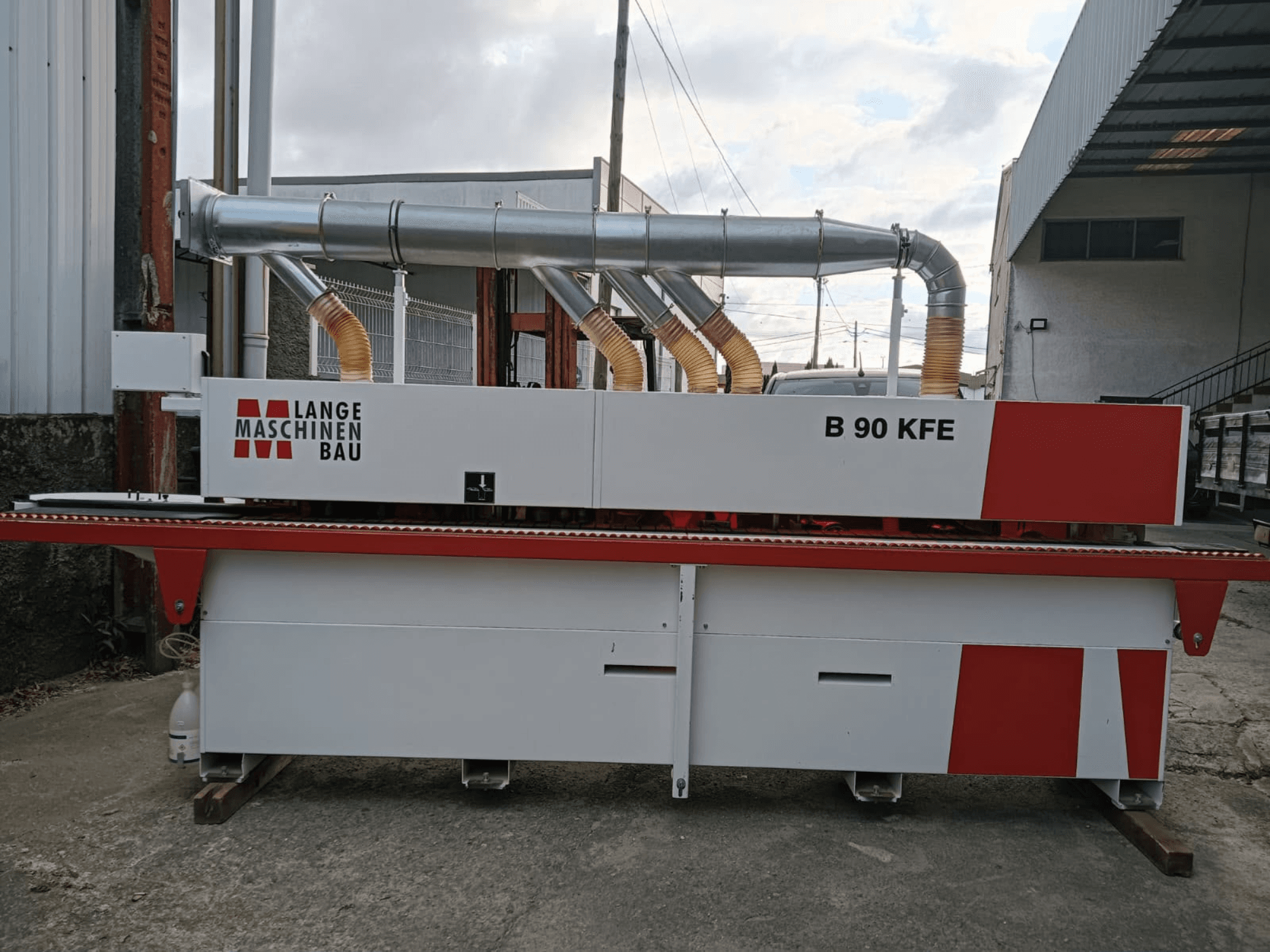 Kantenanleimmaschine LANGE Maschinenbau B 90 KFE in Seitenansicht mit zwei Auspuffrohren und roten Akzenten, eingebettet in einen industriellen Arbeitsbereich.