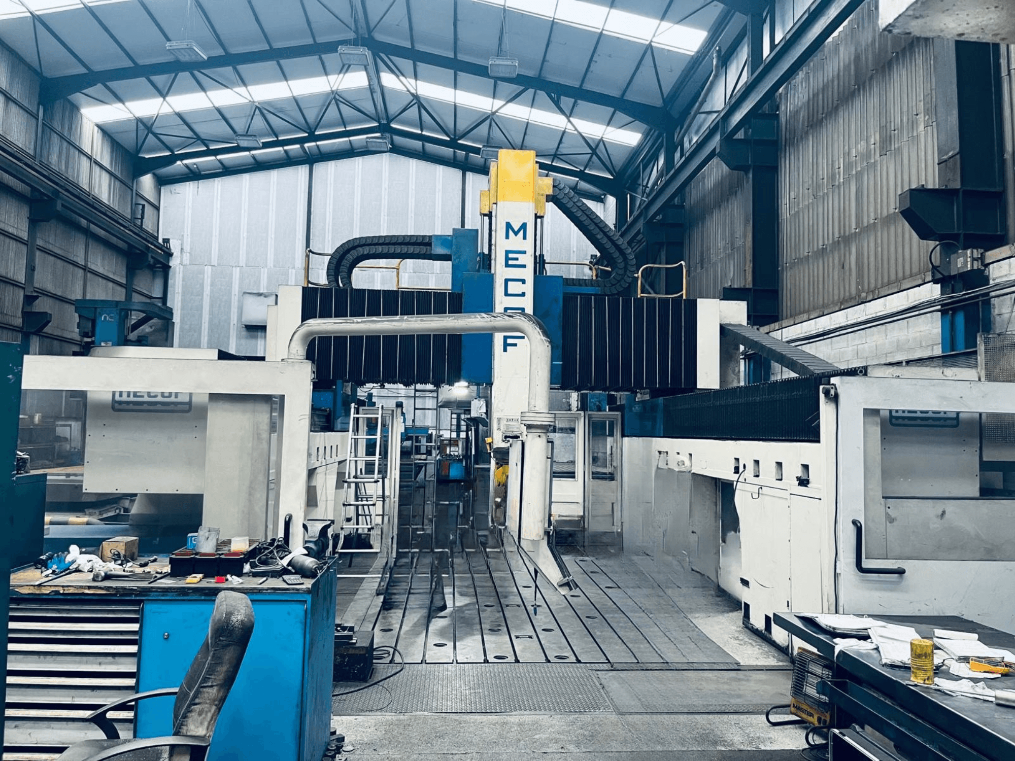 Portalfräsmaschine MECOF DYNAMILL 3000L in der Werkstatt, Vorderansicht, mit blau-weißer Konstruktion, Werkzeugen und Arbeitsbereich.