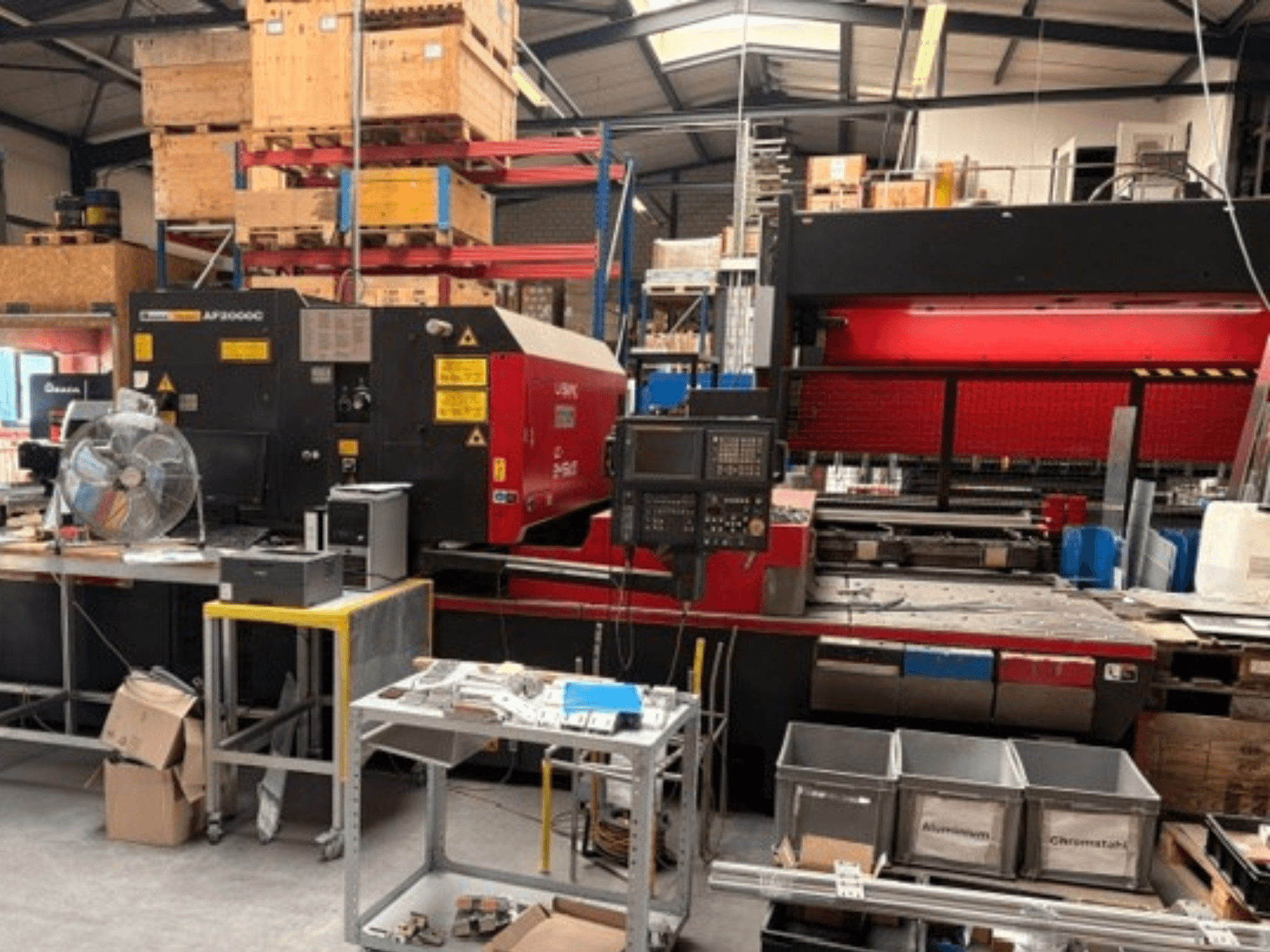 AMADA LC-2415αIII CO₂-Laserschneidmaschine in einer Werkstattumgebung, mit Frontansicht, Bedienfeld und Arbeitsbereich.