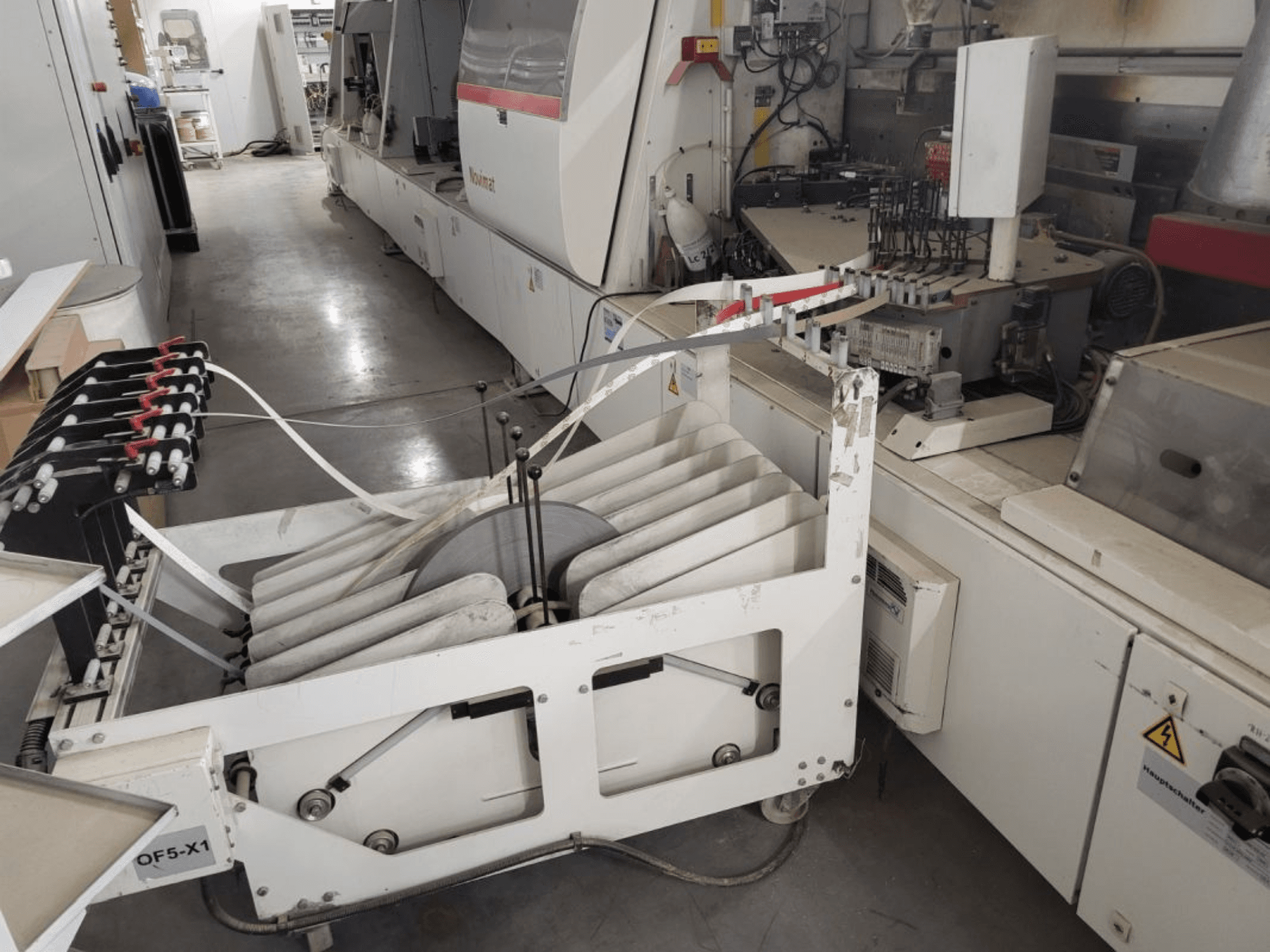 IMA Novimat/I/680/650/R3 Kantenanleimmaschine, Seitenansicht mit Vorschubwalzen und Bedienfeld inmitten einer Werkstattumgebung.