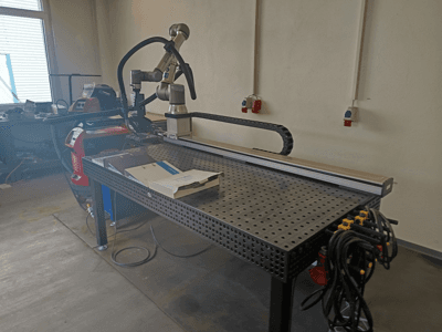 FRONIUS TransSteel 4000 Impulsschweißzelle in Seitenansicht, mit Roboterarm, Arbeitsbereich und Stromanschlüssen.