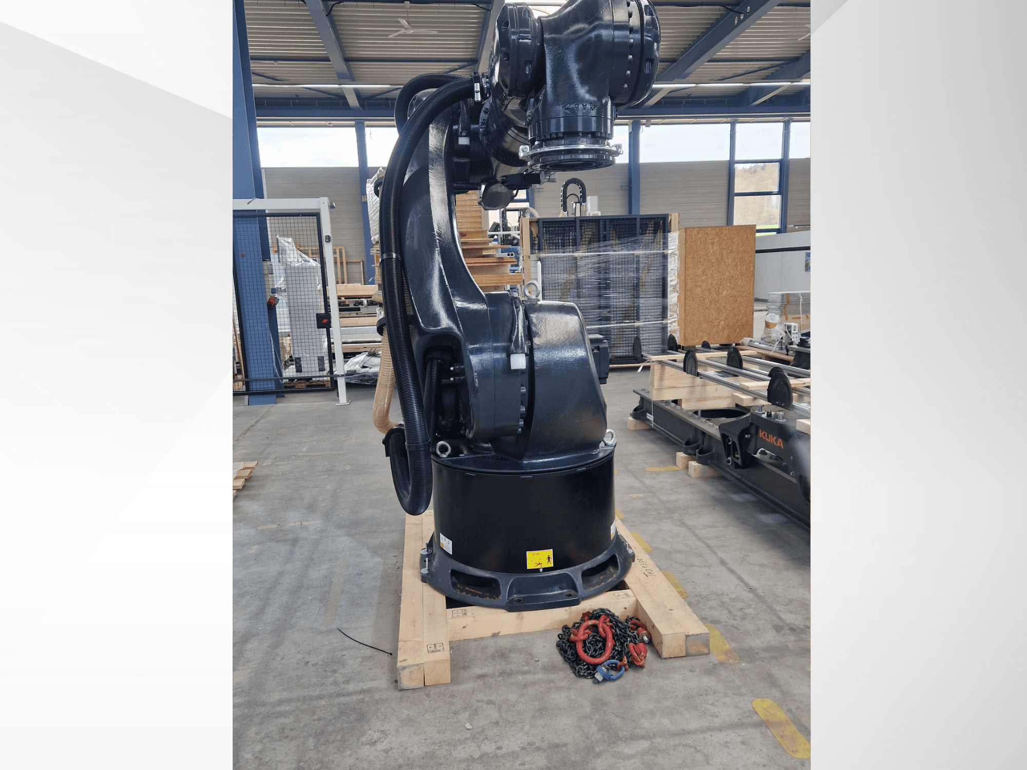 KUKA KR 340 R3330-Roboterarm in einem Lager, Seitenansicht mit Sockel und Kabeln, im Vordergrund Ketten.