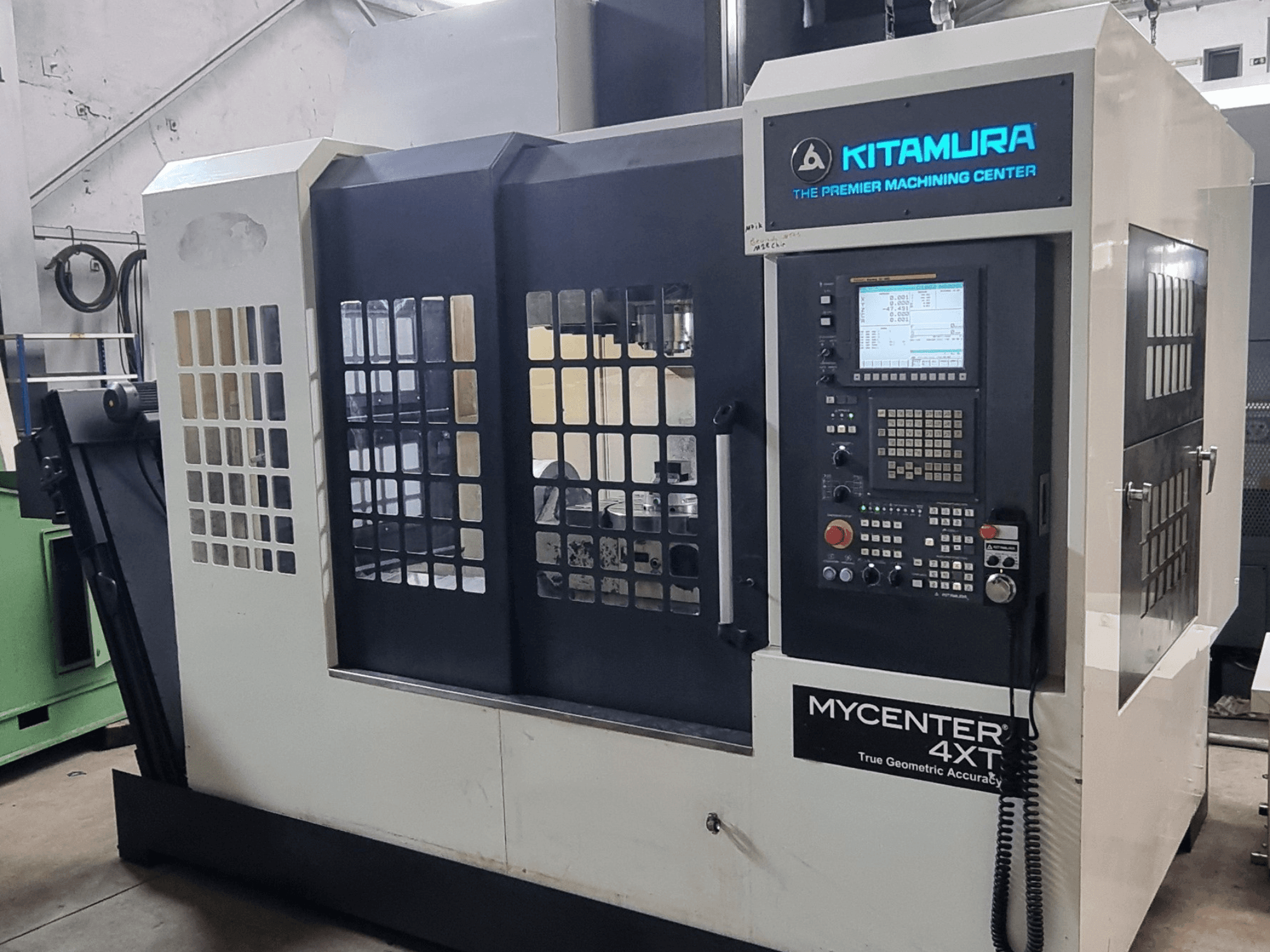 Alternativtext: Vertikales Bearbeitungszentrum Kitamura MYCENTER 4XT, Vorderansicht, mit Blick auf das Bedienfeld und Details der Maschine in einer Werkstattumgebung.
