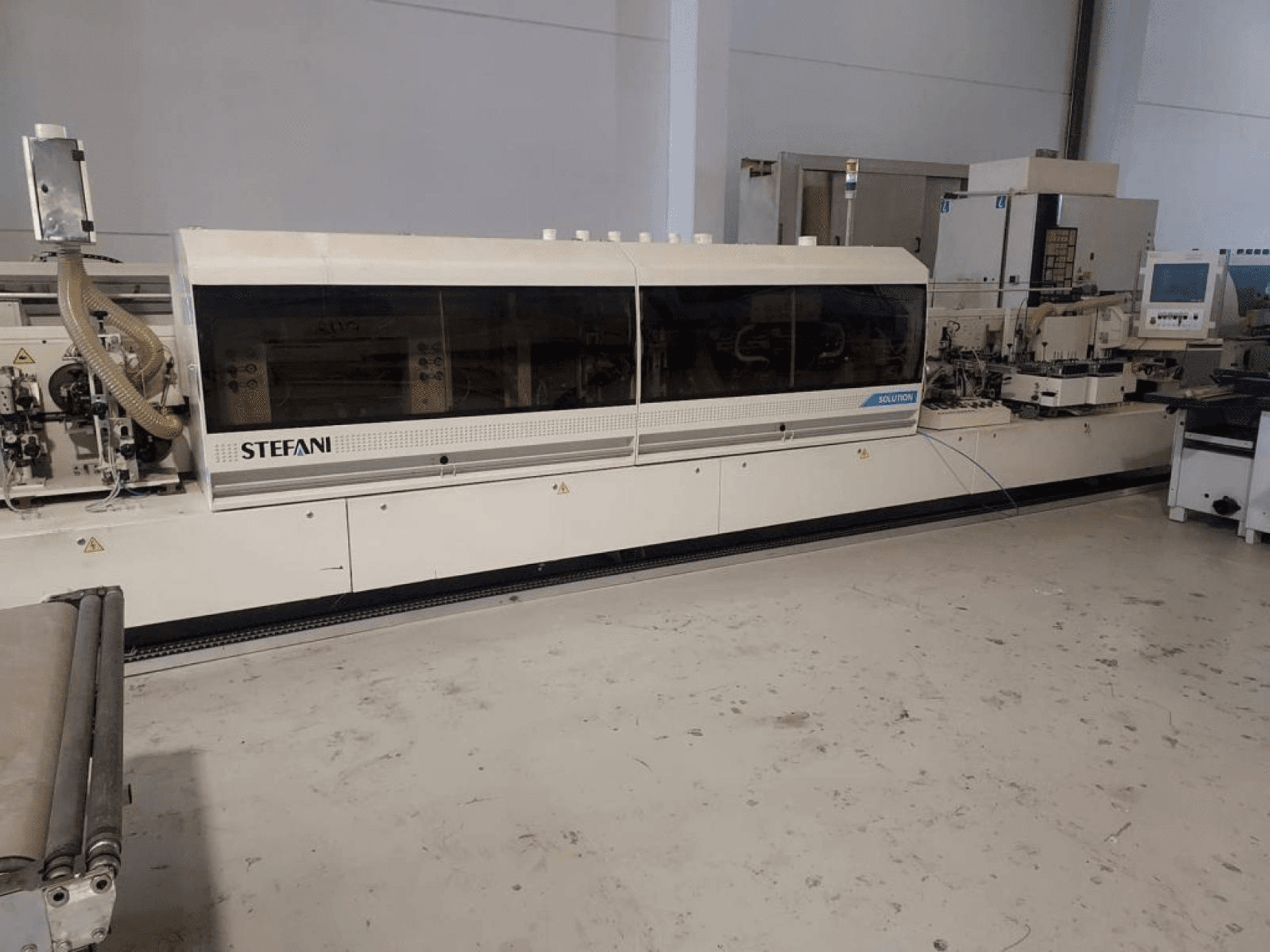 Stefani Solutions Kantenanleimmaschine, Vorderansicht, mit Staubabsaugung und Bedienfeld sichtbar, in einer Werkstattumgebung.