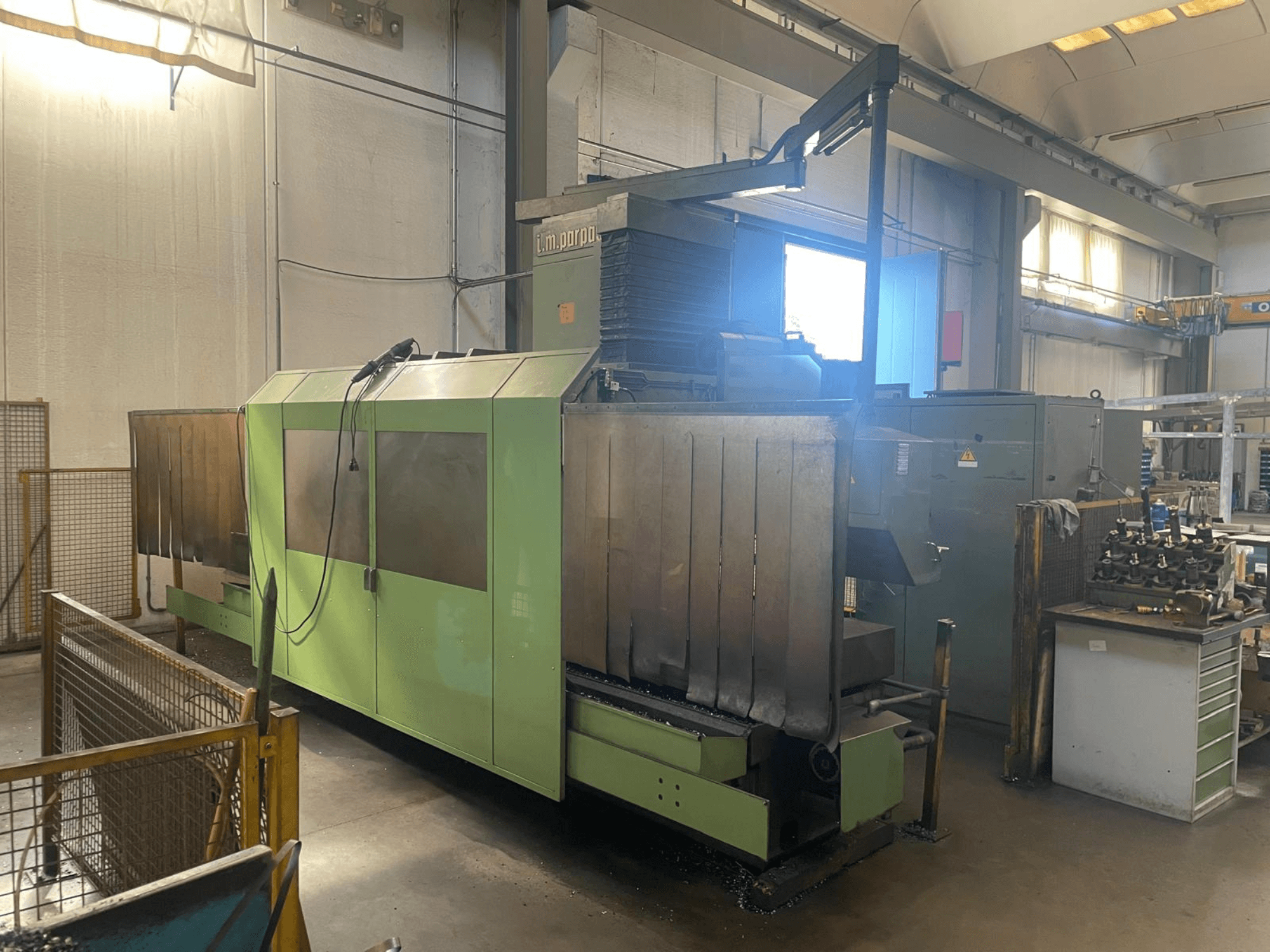 Grüne Industriemaschine mit sichtbaren Metallteilen, Vorderansicht; mit Bedienfeld, Sicherheitswarnungen und Arbeitsplatz in der Nähe.