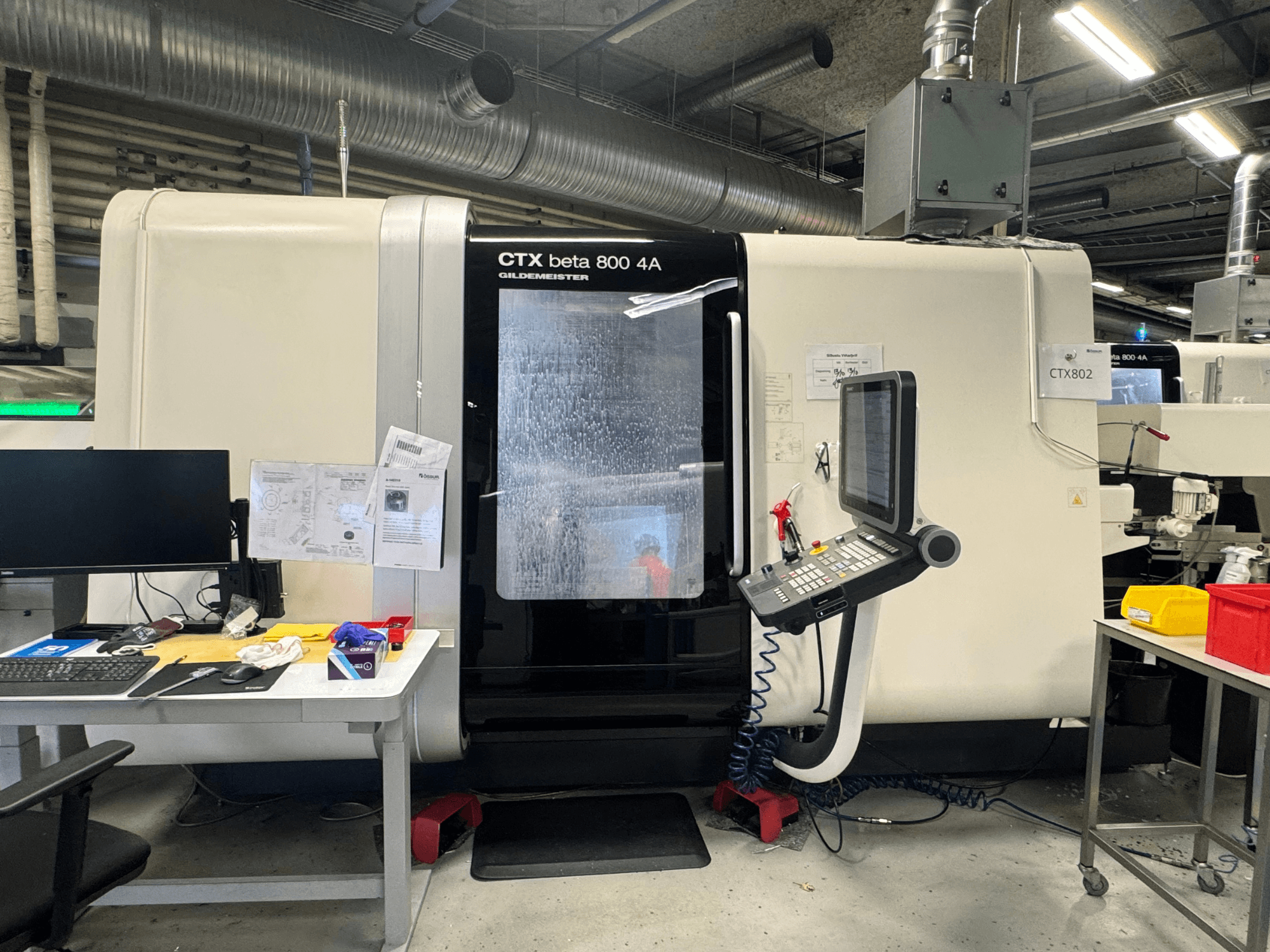 CNC-Maschine CTX beta 800 4A in einer Werkstatt, Seitenansicht mit Bedienfeld und Arbeitsbereich, der mit Werkzeugen und Unterlagen vollgestopft ist.