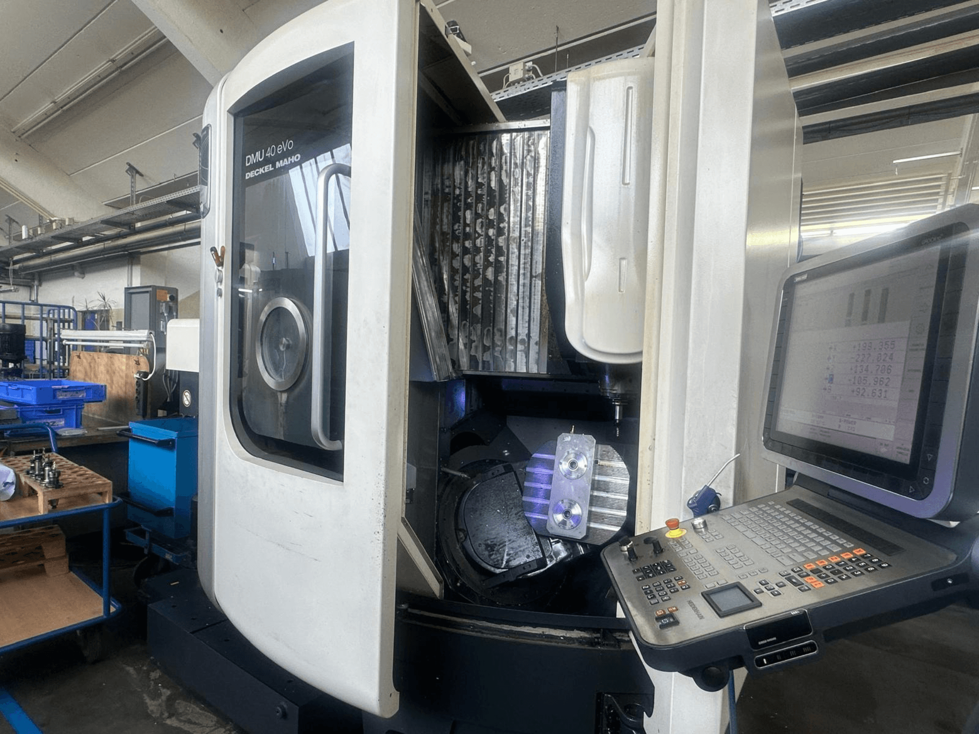 DMU 40 eVo Fräsmaschine von Deckel Maho in einer Werkstatt, Vorderansicht, mit Bedienfeld und Metallstück in der Spindel.