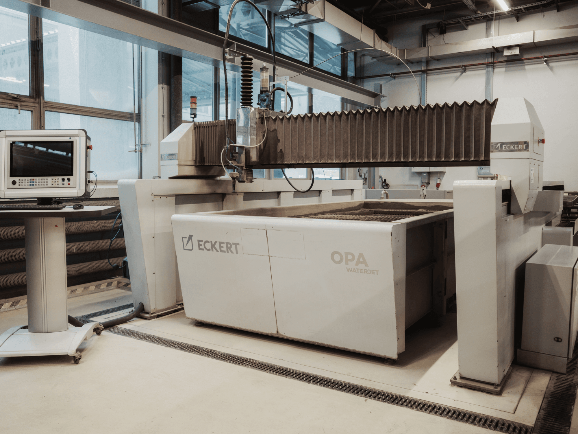 ECKERT OPAL Wasserstrahlschneidemaschine in einer Werkstatt, von vorne gesehen, mit der Steuerkonsole daneben.