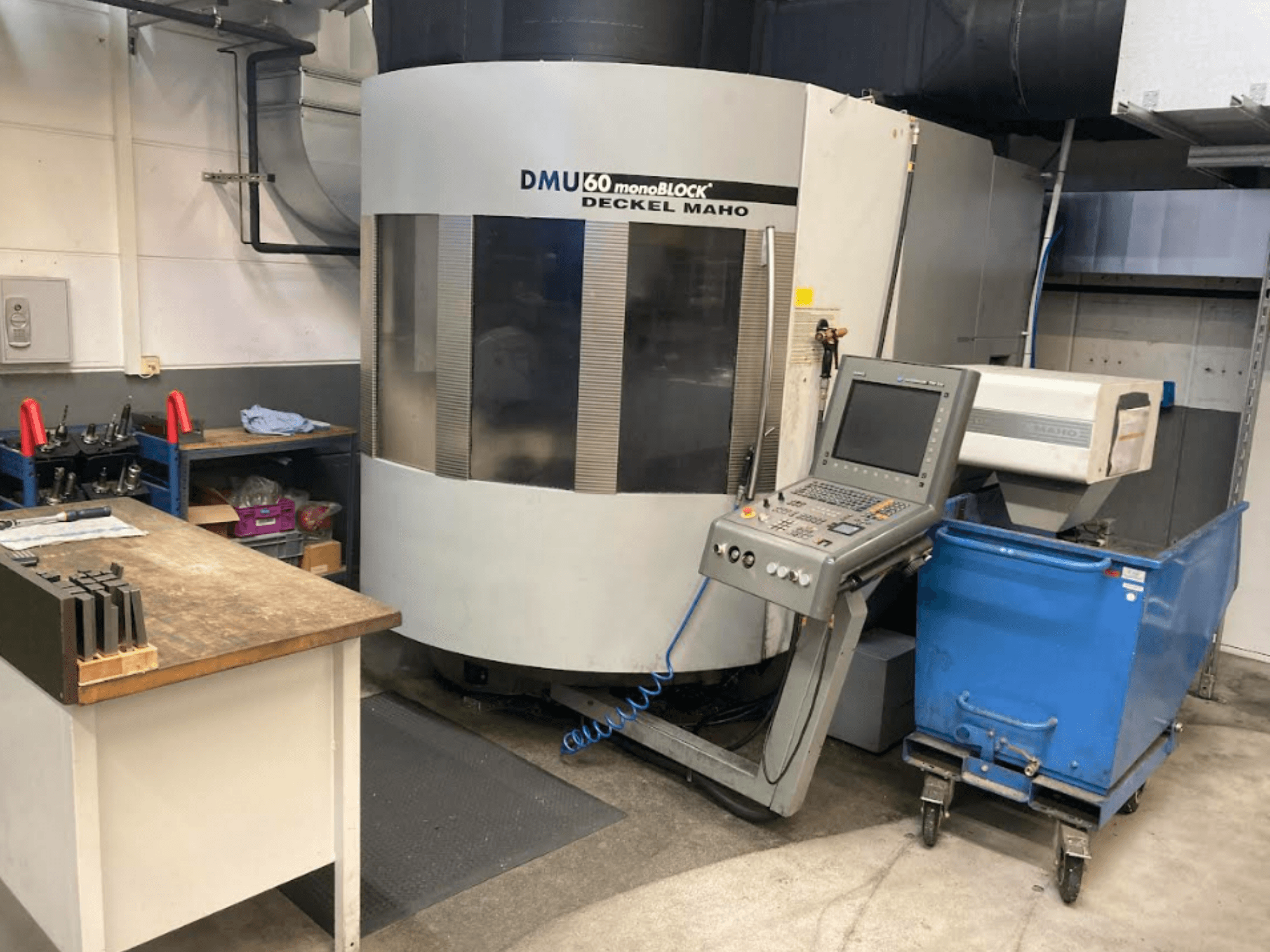 DMG MORI DMU 60 Monoblock Vertikal-Bearbeitungszentrum, Vorderansicht mit Bedienfeld, Arbeitsbereich und blauem Werkzeugwagen.