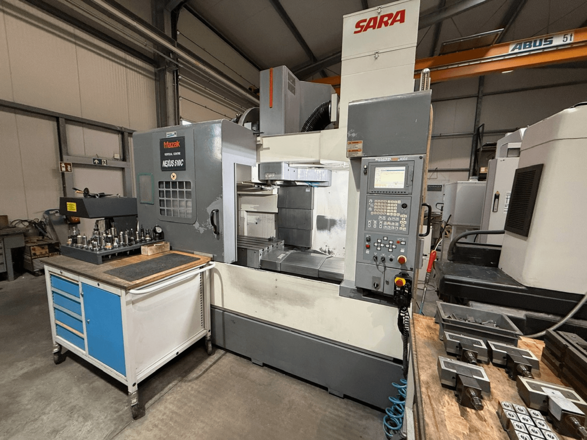 Mazak Nexus 510C Vertikal-Bearbeitungszentrum, Vorderansicht, mit Werkzeugen auf einem Wagen; SARA-Branding sichtbar; technische Bedienelemente dargestellt.