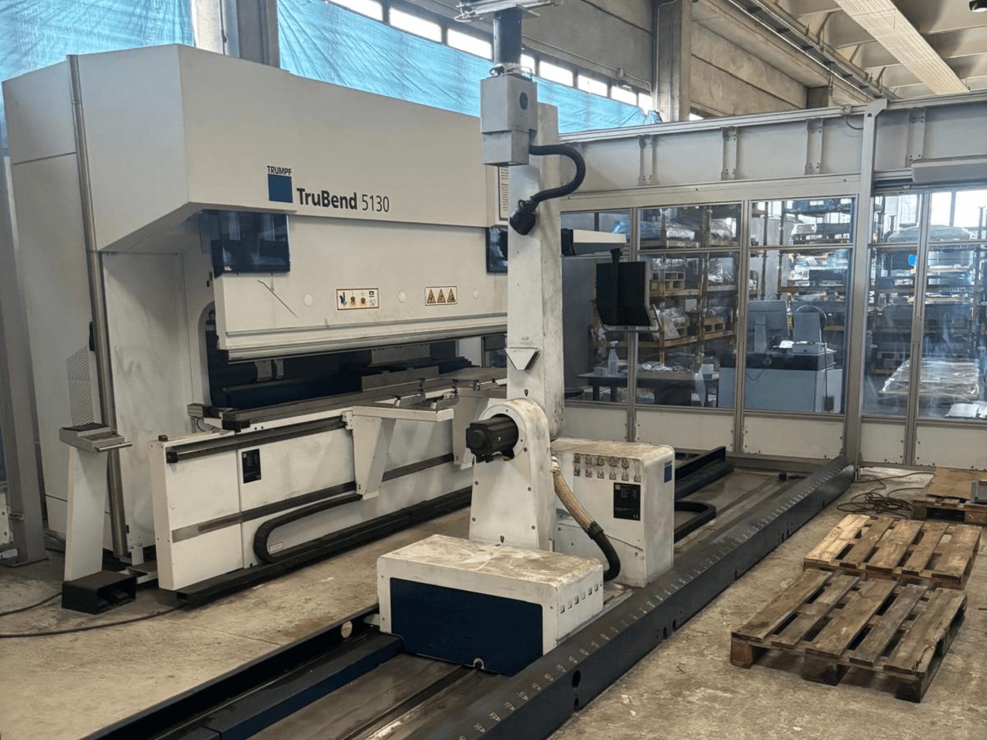 TruBend 5130 Biegemaschine von Trumpf, Vorderansicht, mit Bedienpult und Paletten in einer Werksumgebung.