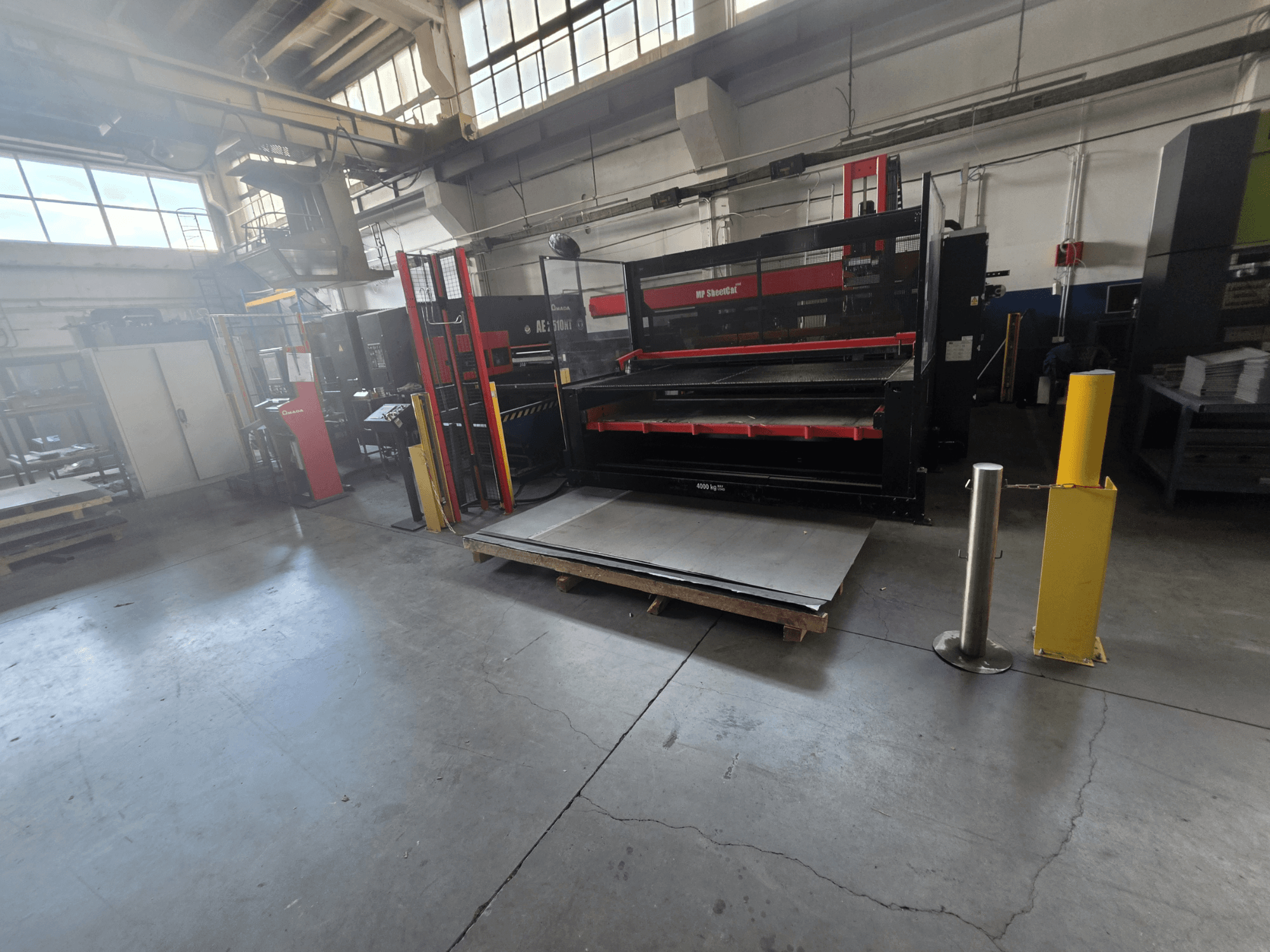 CNC-Stanzmaschine AMADA AE-2510NT im Lager, aus seitlichem Blickwinkel aufgenommen, mit Blick auf die Maschinenaufstellung und die Bleche.