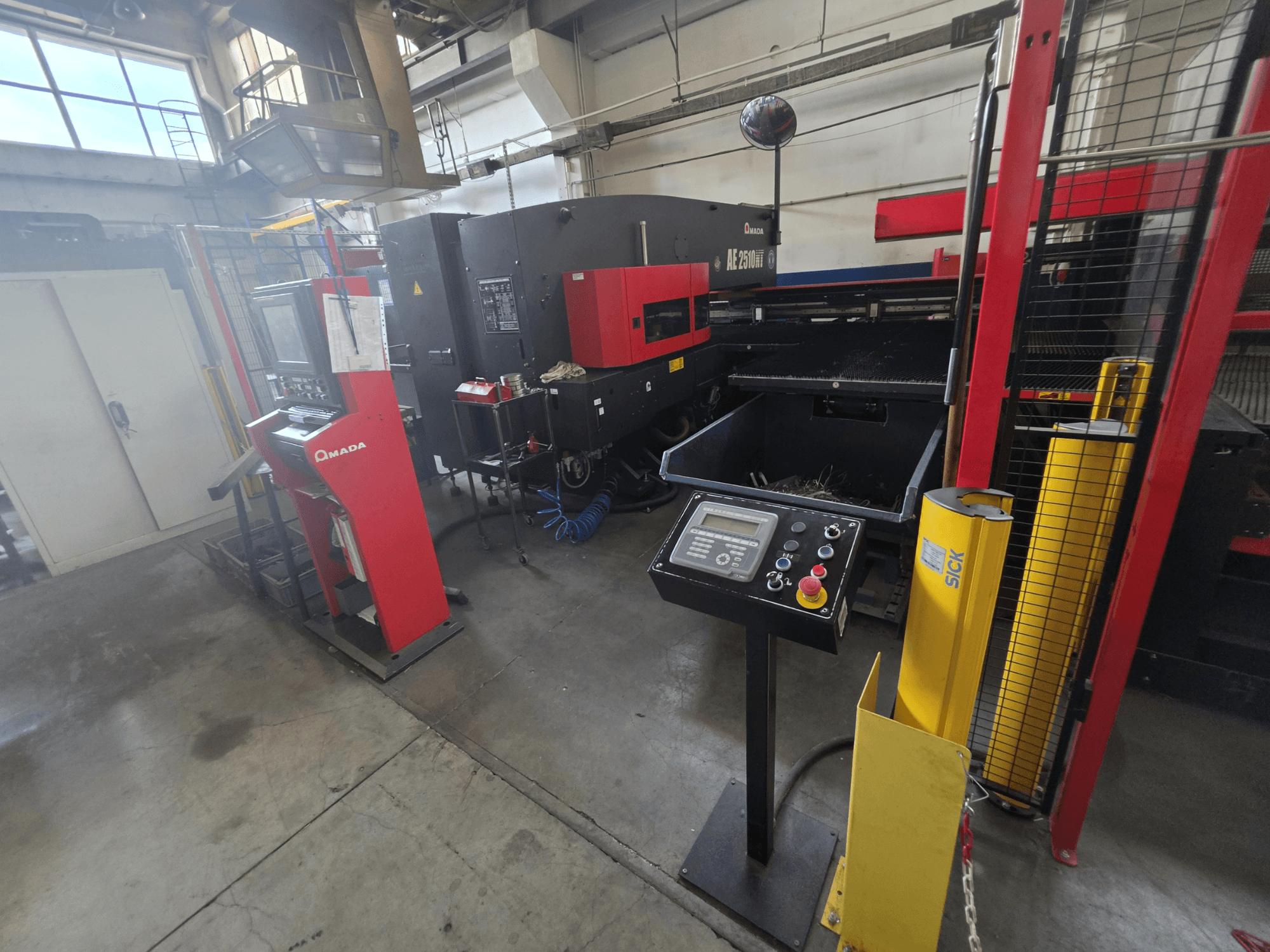 CNC-Stanzmaschine AMADA AE-2510NT, Vorderansicht mit Bedienfeld, Sicherheitsvorrichtungen und der umgebenden Industrieumgebung.