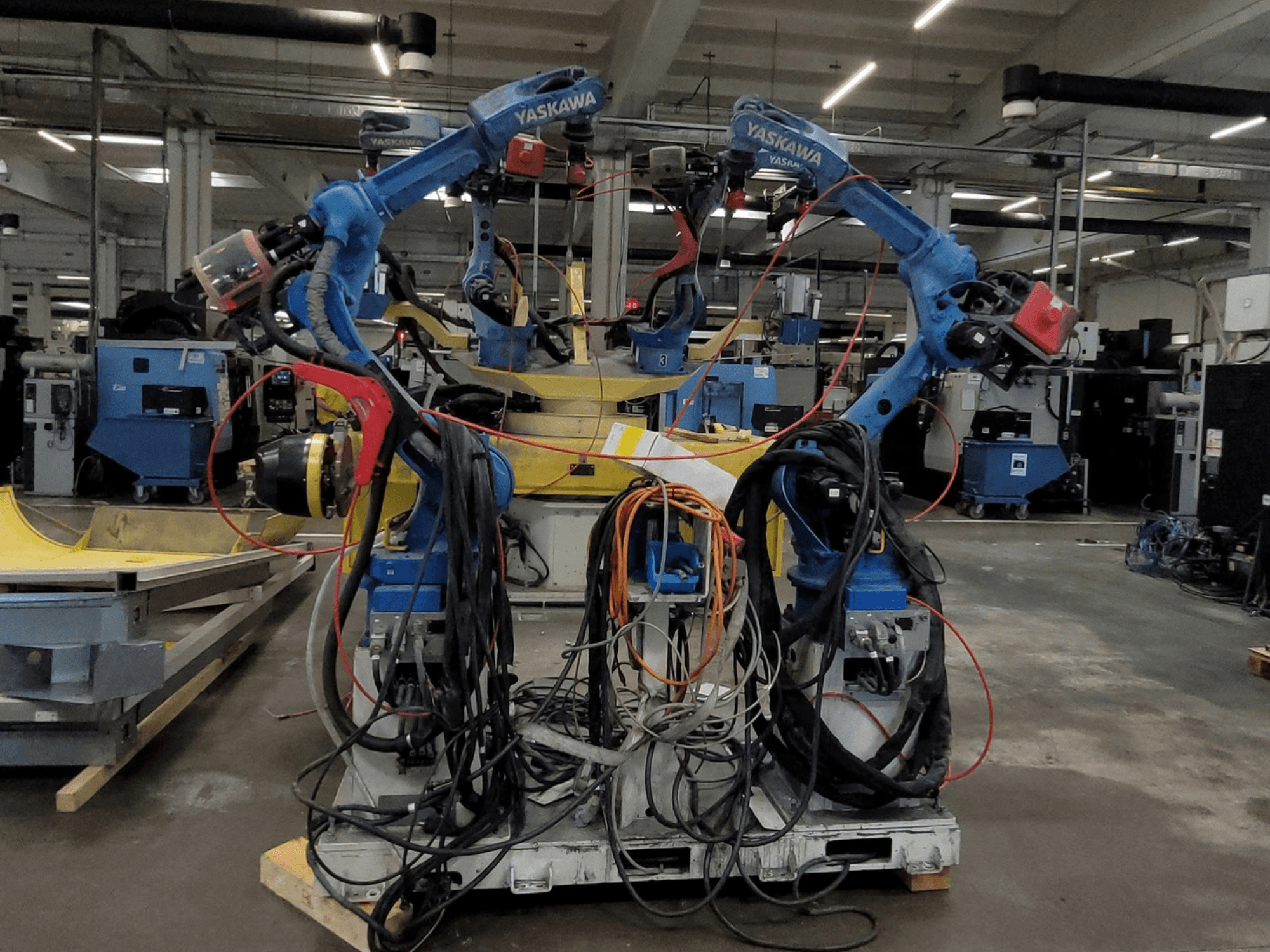 Yaskawa-Schweißroboterzelle RWC L1_OS 15330, Vorderansicht, mit zwei blauen Robotern, zahlreichen Kabeln und Schweißwerkzeugen.