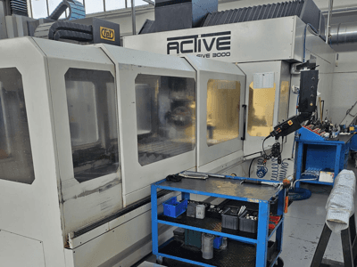 Aktive CNC-Maschine 3000 in einer Werkstatt, Vorderansicht mit Werkzeugen auf einem blauen Wagen, sichtbare Bedienelemente und Arbeitsbereich im Inneren.