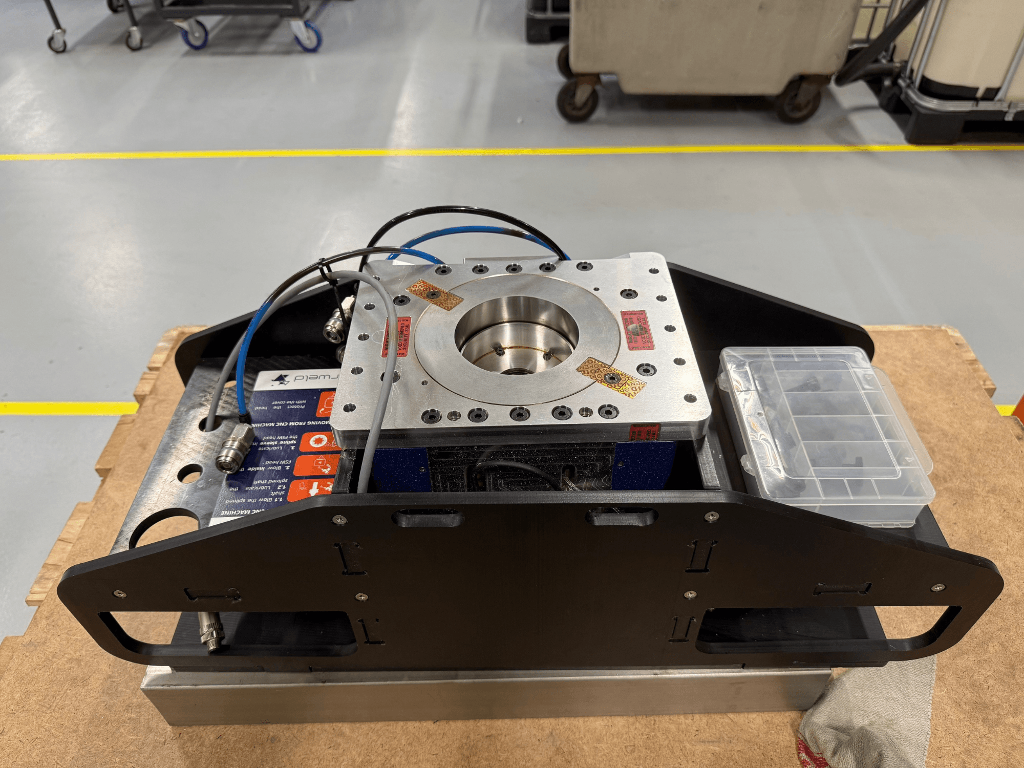 Bearbeitete Metallkomponente mit blauen Kabeln, Zubehörkoffer und flachem Sockel, von oben gesehen, ideal für mechanische Anwendungen.