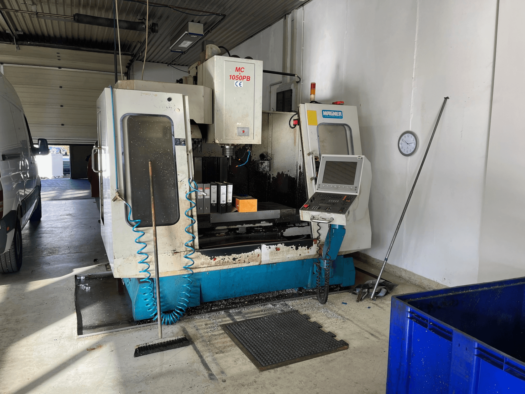 WAGNER MC 1050PB CNC-Maschine in der Werkstatt, Vorderansicht, mit Bedienfeld und Arbeitsbereich; blauer Luftschlauch und Reinigungswerkzeuge sichtbar.
