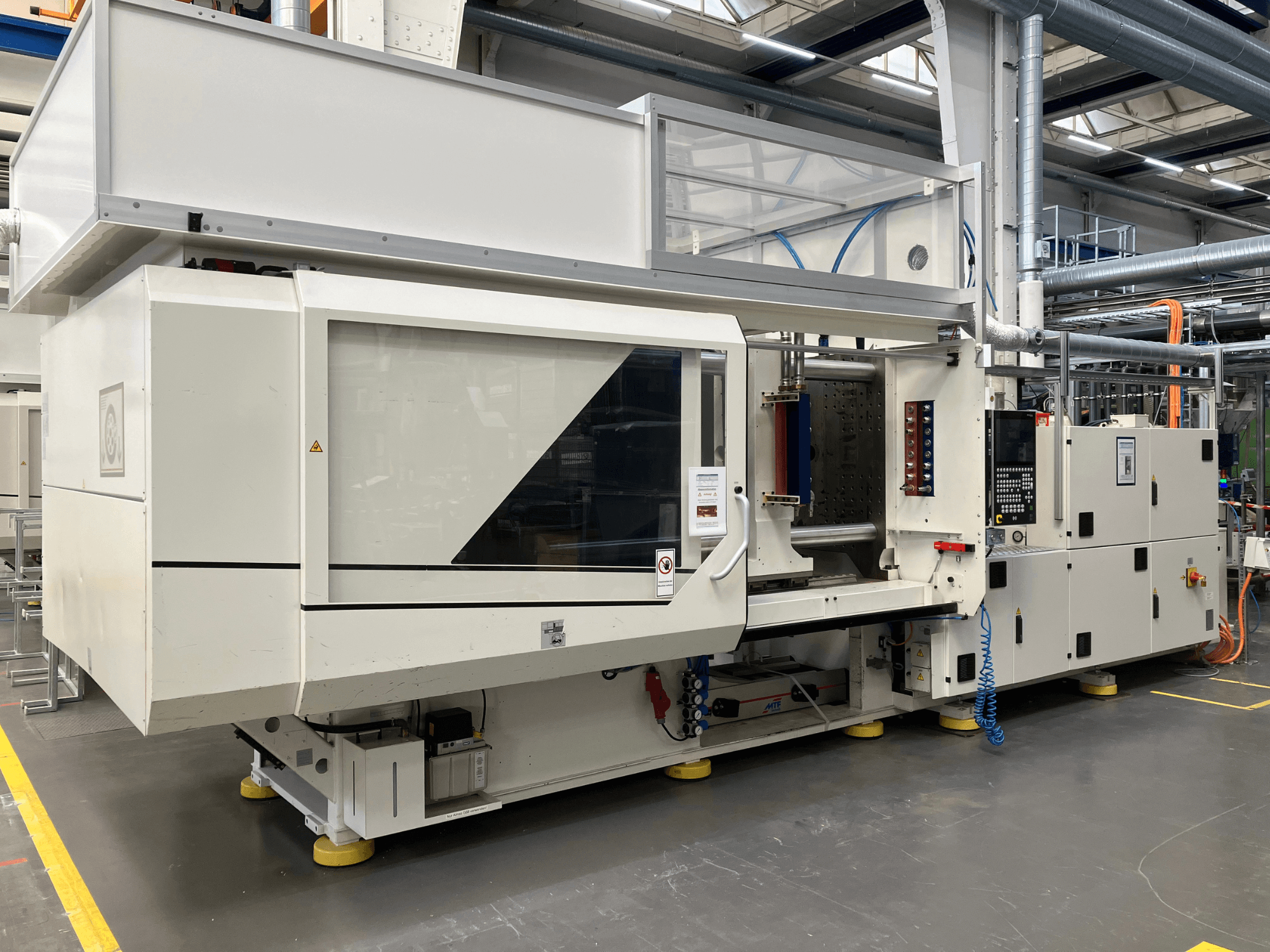 Seitenansicht einer Spritzgießmaschine, Modell AET, mit Bedienfeld und transparenten Abdeckungen, in einer industriellen Umgebung.