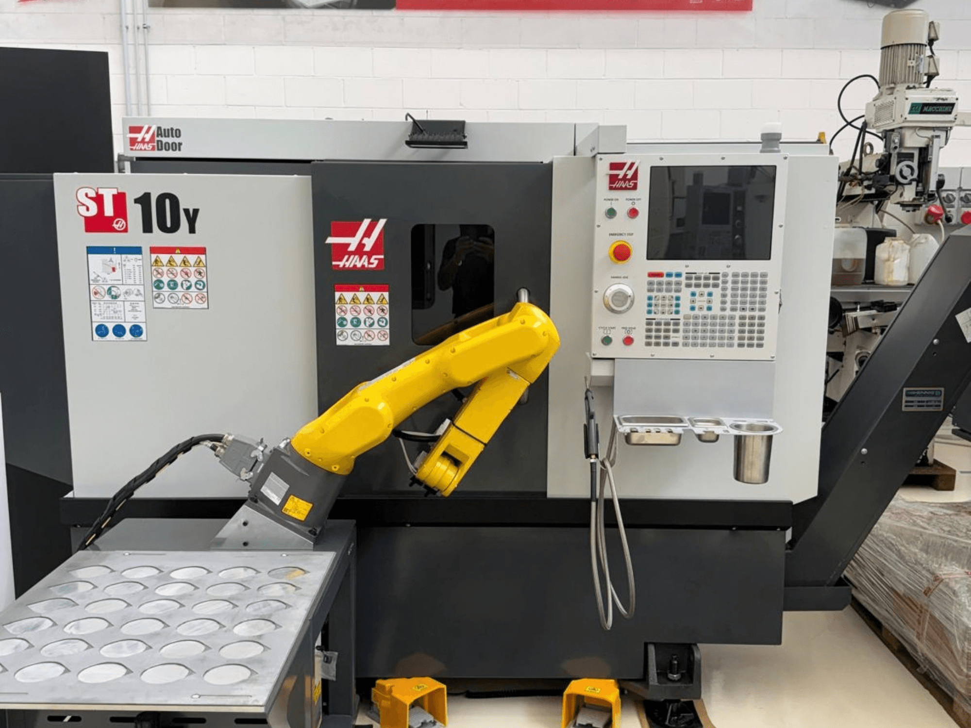 Die horizontale Drehmaschine Haas ST-10Y von vorne gesehen, ausgestattet mit einem Roboterarm und einem Bedienfeld mit Werkzeughalter-Einsätzen.