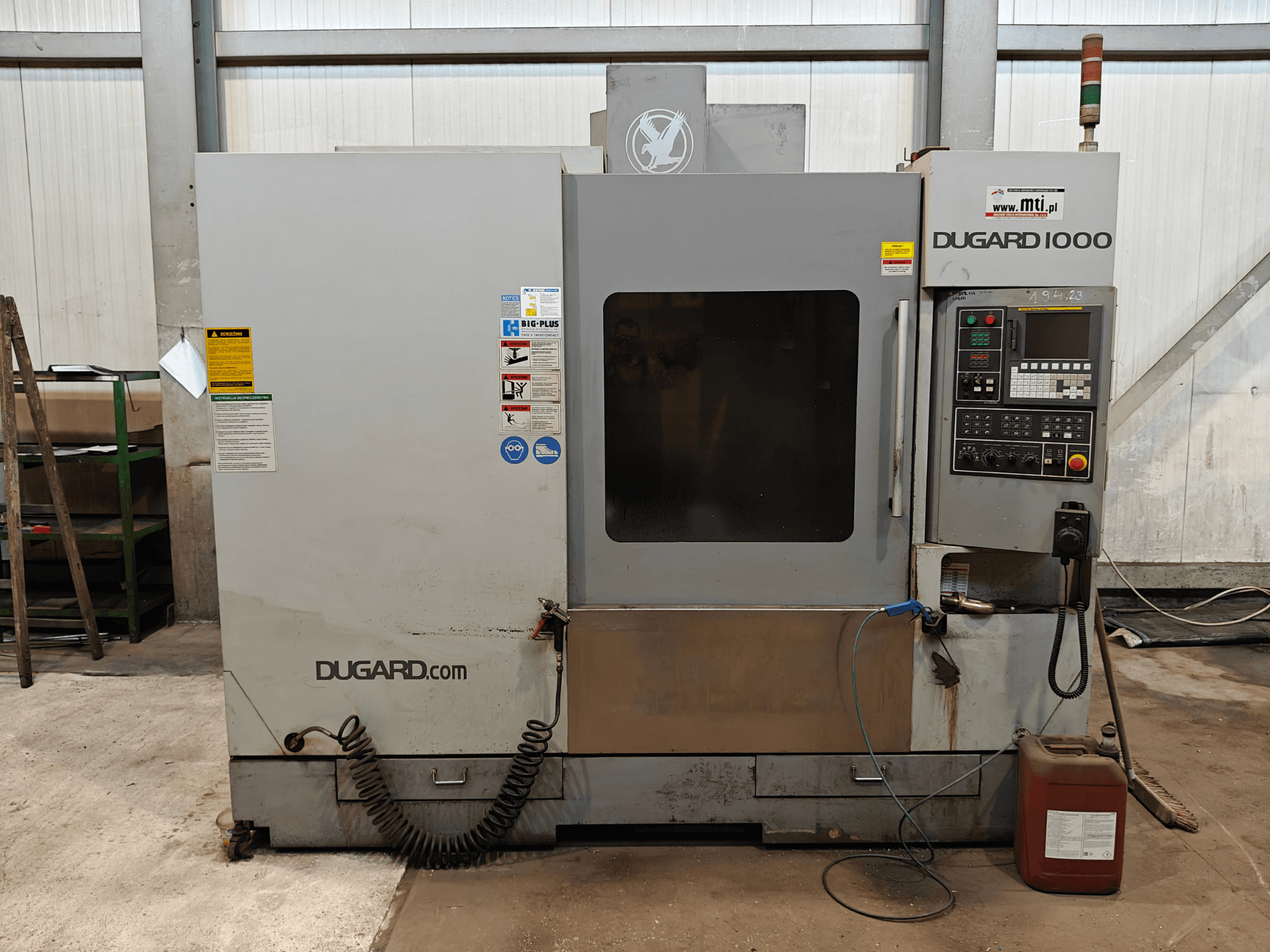 Dugard 1000 CNC-Maschine, Vorderansicht, mit Bedienfeld, Sicherheitsschildern und Ölbehälter, in einer Werkstatt.