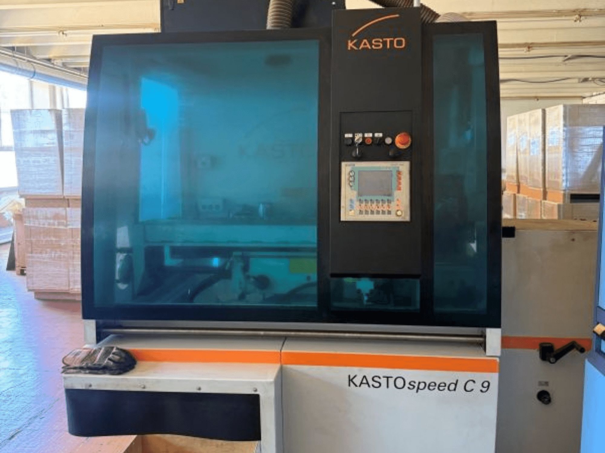 Vorderansicht der KASTO KASTOspeed C 9 Kreissäge für Metall, mit Bedienfeld und Sicherheitsglas, im Hintergrund sind Holzkisten zu sehen.
