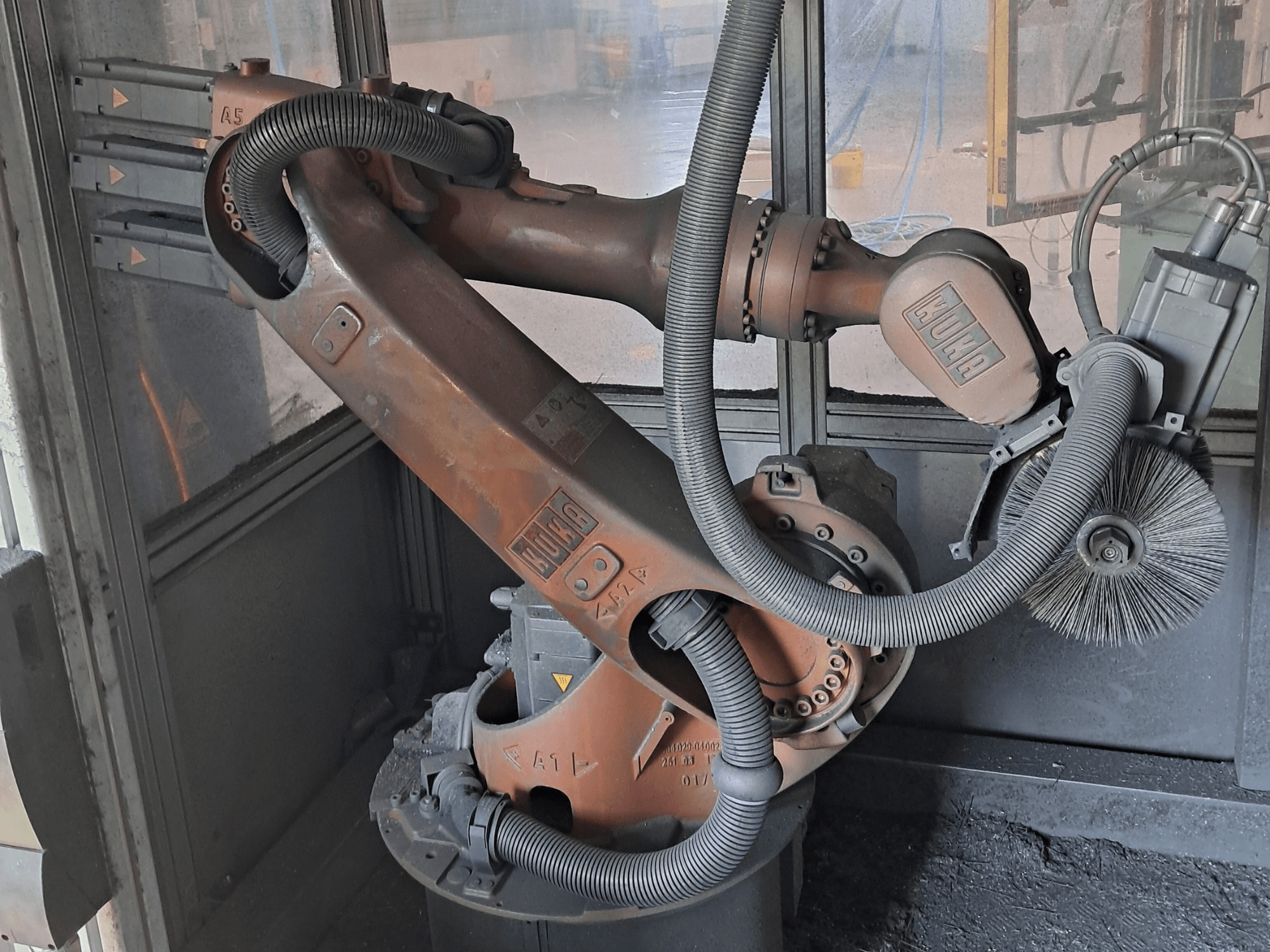 Der Roboterarm KUKA KR 16-2 in Seitenansicht, der Kabel, Bürsten und mechanische Gelenke zeigt, eingebettet in eine Arbeitsumgebung.