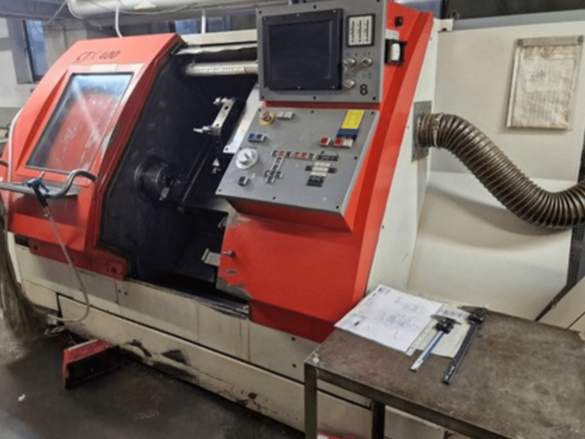Gildemeister CTX 400 Horizontaldrehmaschine, Vorderansicht mit Bedienfeld und Absaugschlauch. Inklusive Messwerkzeuge auf dem Tisch.
