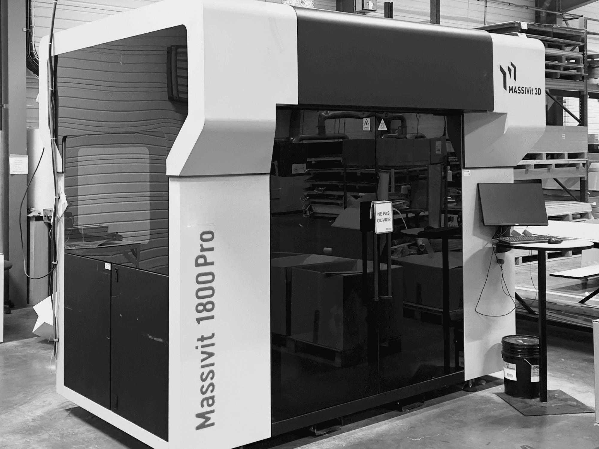 Der Kunststoff-3D-Drucker MASSIVIT 1800 PRO in einer Werkstatt, Vorderansicht, mit sichtbarem Computerarbeitsplatz und Bedienfeld.