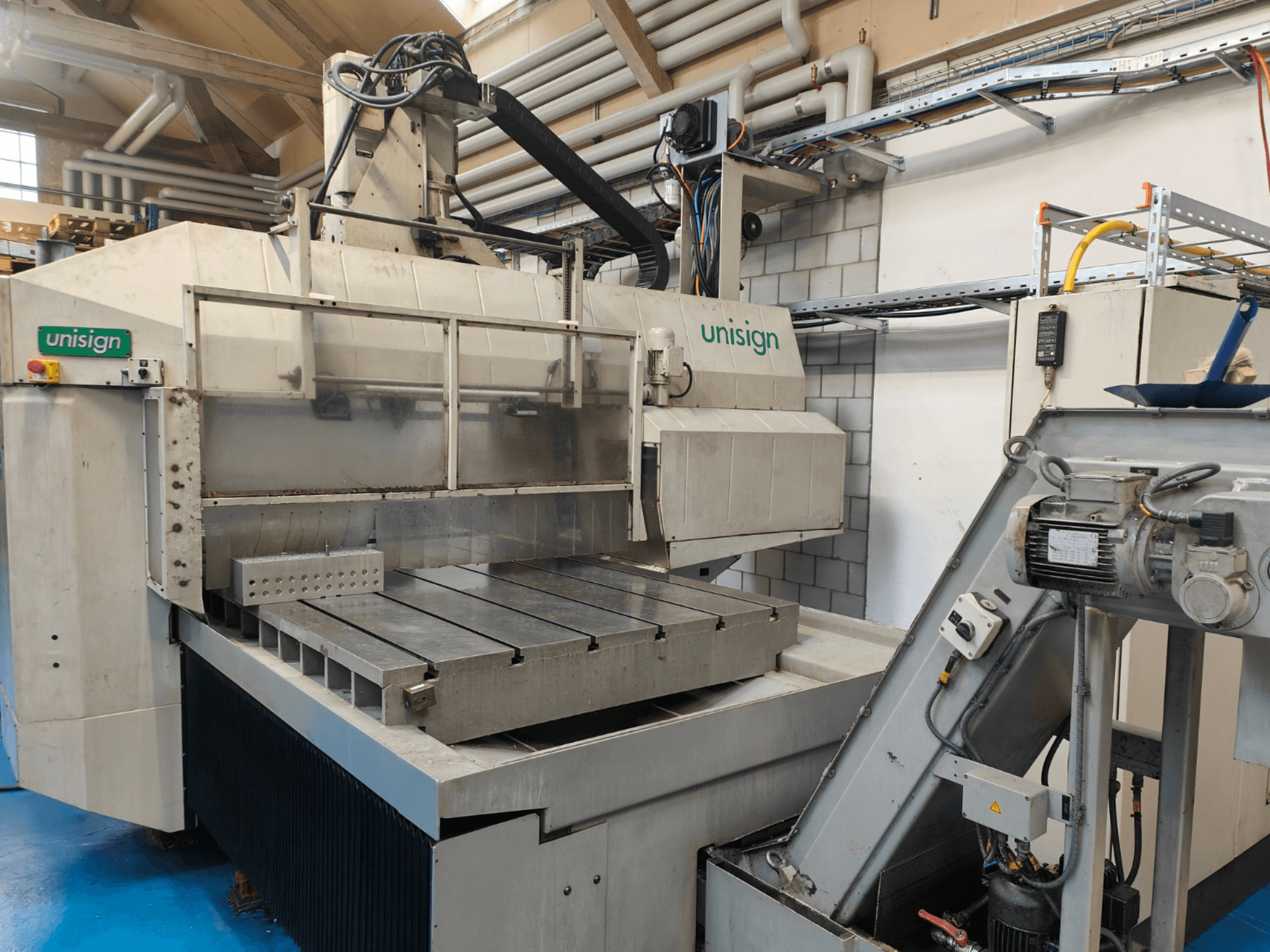 Unisign CNC-Maschine in einer Werkstatt, Vorderansicht, mit großem Tisch, Bedienfeld und industriellen Designelementen.