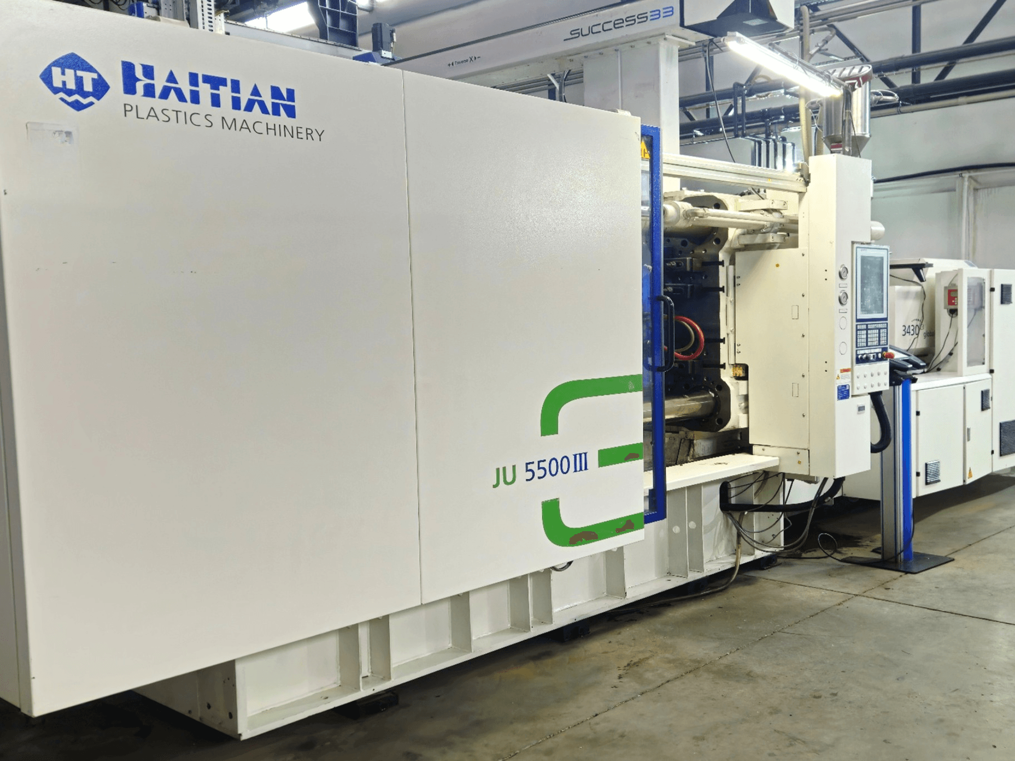 Die haitianische Kunststoffmaschine JU 5500III in einer Fabrikumgebung, Vorderansicht mit Bedienfeld und Produktionsbereich.