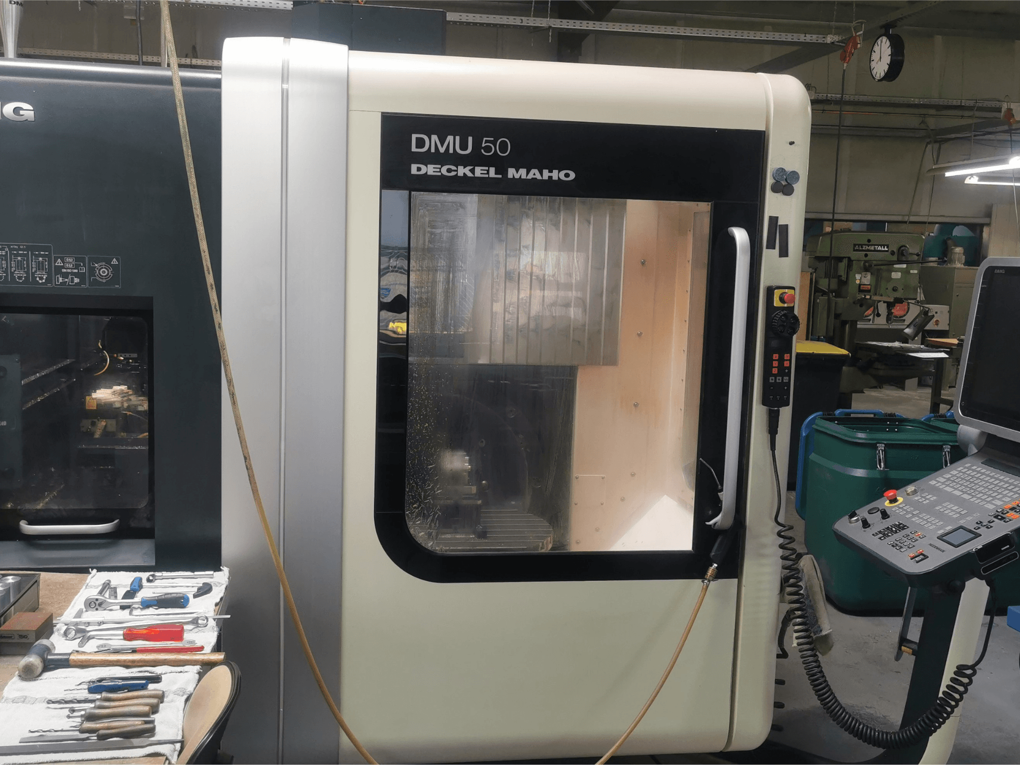 Die CNC-Maschine DMU 50 deckel maho in der Frontansicht mit dem Bedienfeld und der transparenten Tür. Die Werkzeuge sind in der Nähe.